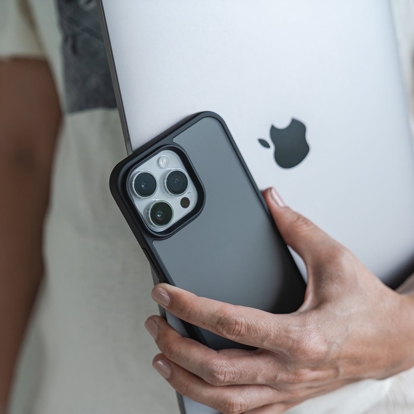 Eine Person hält ein silbernes iPad und ein Smartphone in der MR PROTECT iPhone 15 Hülle Matt von MR PROTECT, die sich durch minimalistische Mattoptik und Stoßdämpfung auszeichnet. Nur der mit einem cremefarbenen Hemd bekleidete Oberkörper und die Hand sind sichtbar.