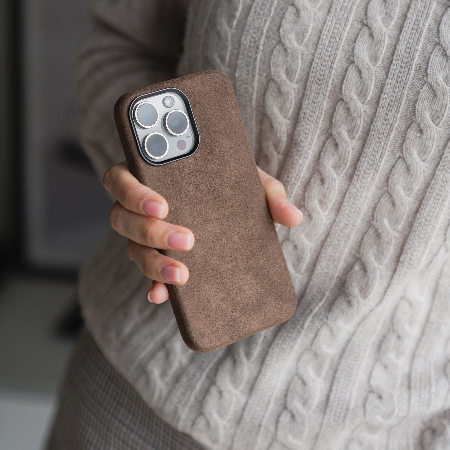 Eine Person hält ein Smartphone in der arktis iPhone Air Hülle aus Alcantara von arktis und trägt einen beigen Zopfstrickpullover.