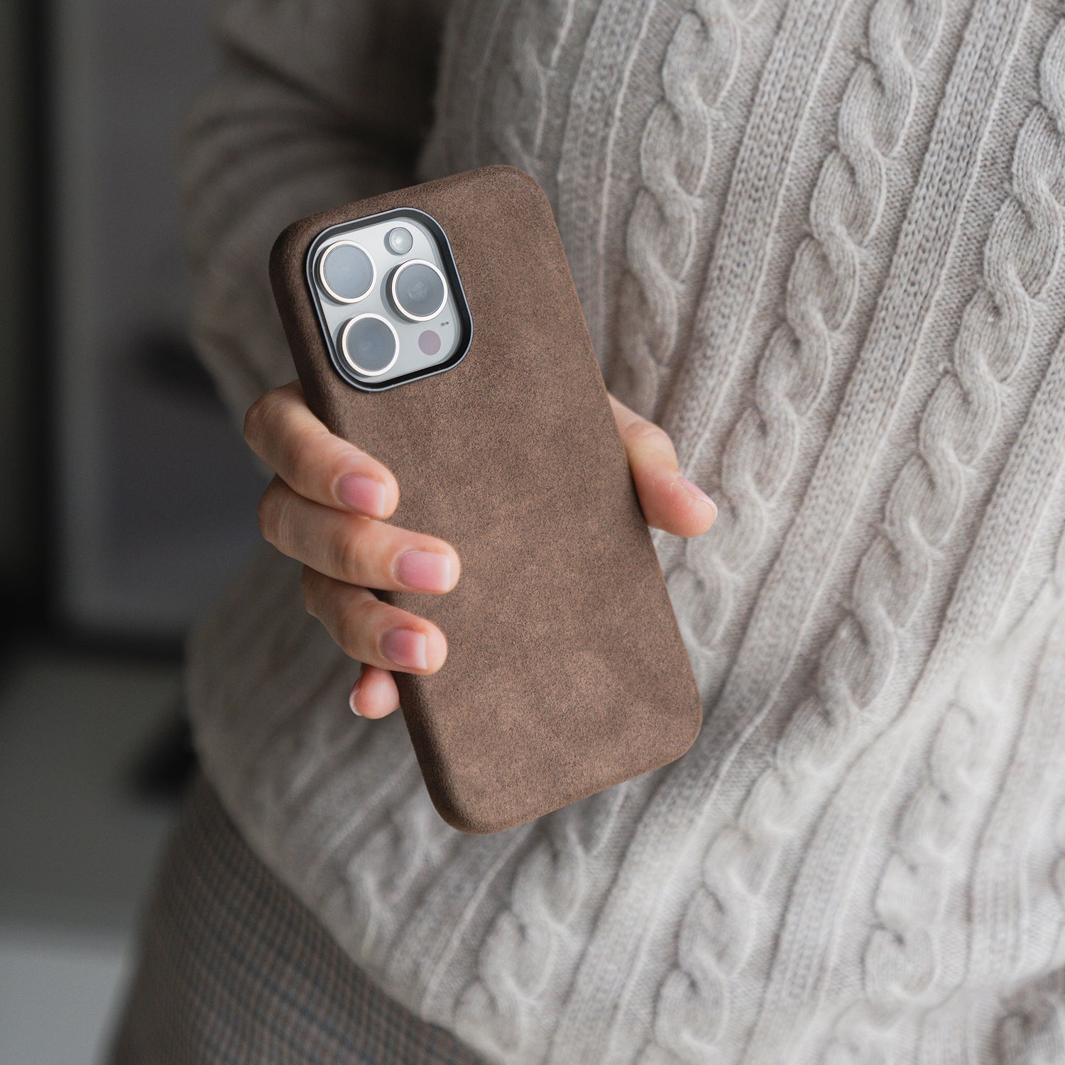 Eine Person hält ein Smartphone in der arktis iPhone Air Hülle aus Alcantara von arktis und trägt einen beigen Zopfstrickpullover.