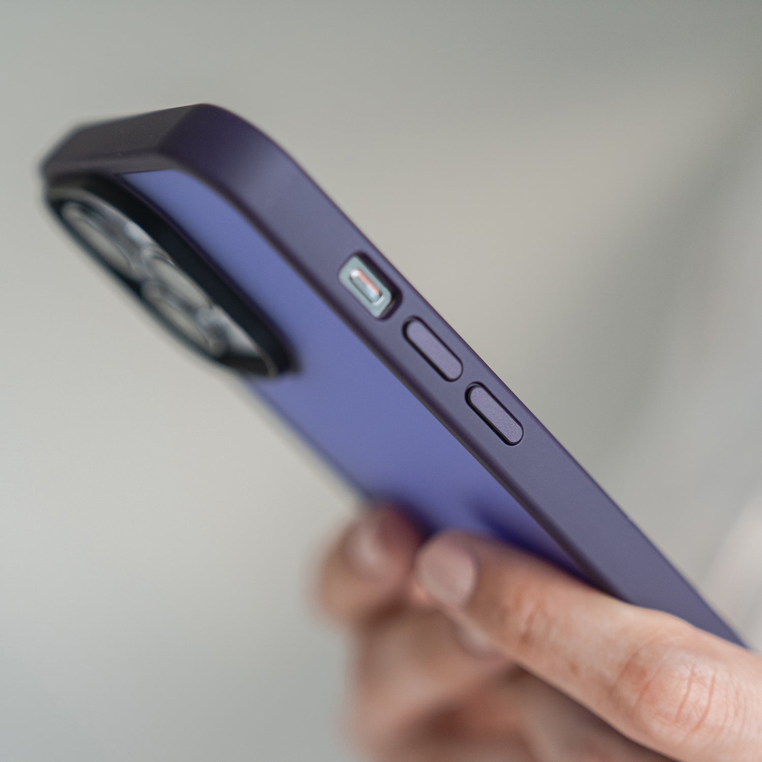 Die Hand einer Person hält das MR PROTECT iPhone 15 Pro Case Matt von MR PROTECT, eine violette, stoßdämpfende TPU-Silikonhülle, die die Seitentasten und das Kameramodul vor einem schlichten Hintergrund zeigt.