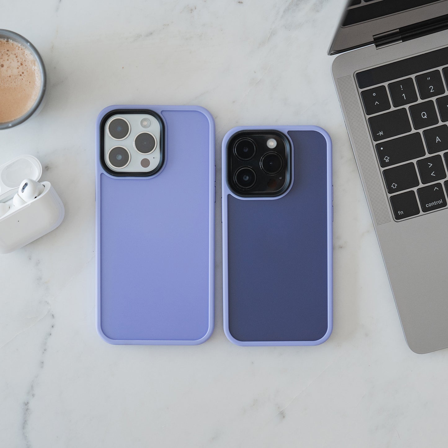 Zwei iPhones in der MR PROTECT iPhone 15 Hülle Matt liegen auf weißem Marmor neben Laptop, kabellosen Ohrhörern und Kaffeetasse – stilvoller Schutz von MR PROTECT mit stoßabsorbierendem, minimalistischem Design.
