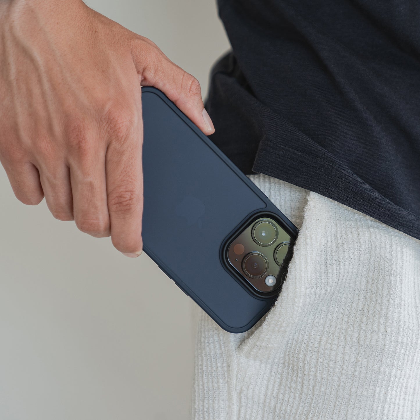 Eine Person in heller Hose und schwarzem Hemd hält ein MR PROTECT iPhone 15 Case Matt in minimalistischer Mattoptik und steckt es teilweise in die Hosentasche.