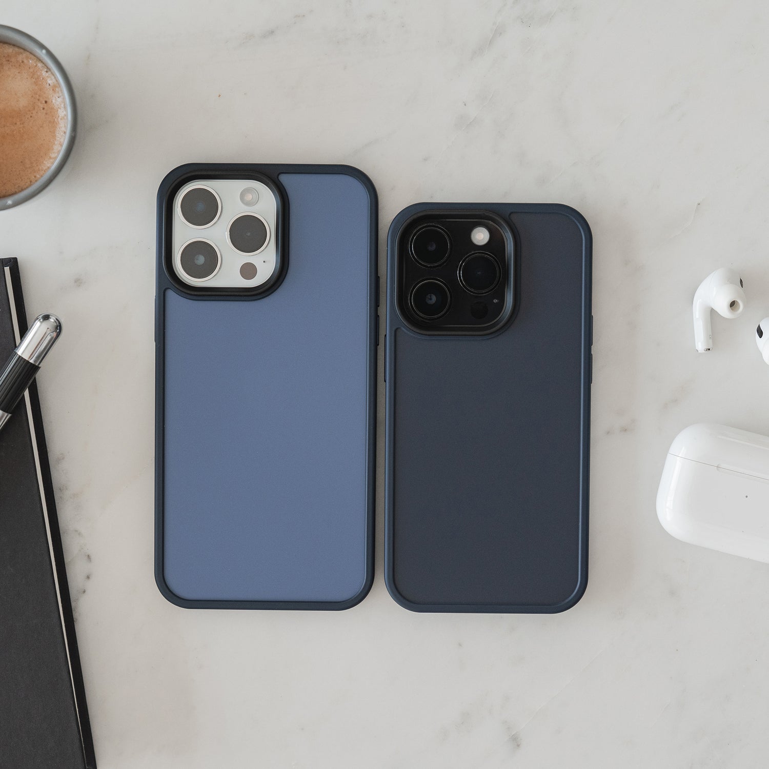 Zwei iPhones mit der MR PROTECT iPhone 15 Pro Case Matt von MR PROTECT im stoßabsorbierenden matten TPU-Silikon liegen nebeneinander auf weißem Marmor, daneben eine Kaffeetasse, ein Notizbuch mit Stift und kabellose Kopfhörer im Case.