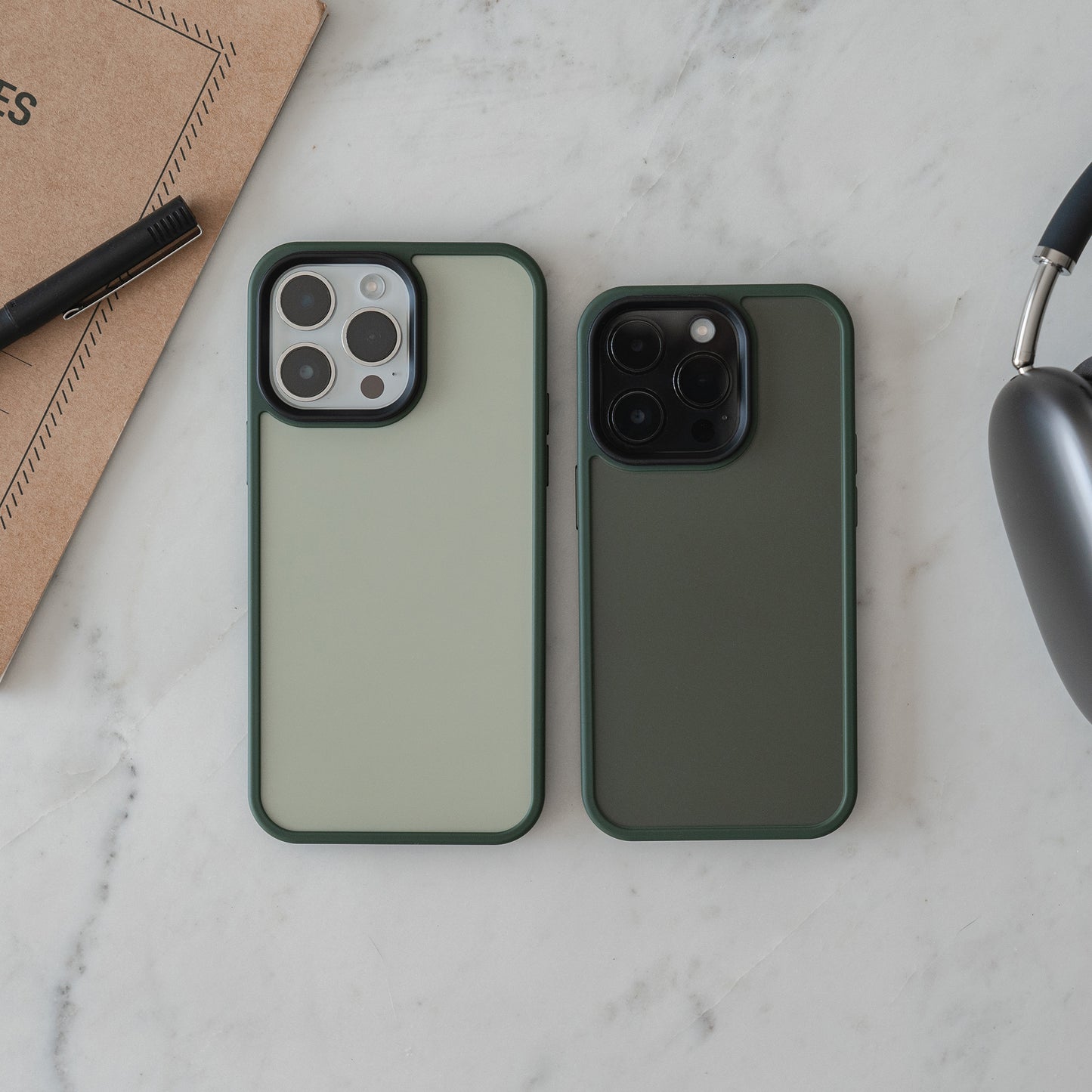 Zwei Smartphones mit der MR PROTECT iPhone 15 Case Matt Hülle von MR PROTECT liegen nebeneinander auf Marmor, umgeben von Notizbuch, Stift und grauen Over-Ear-Kopfhörern.