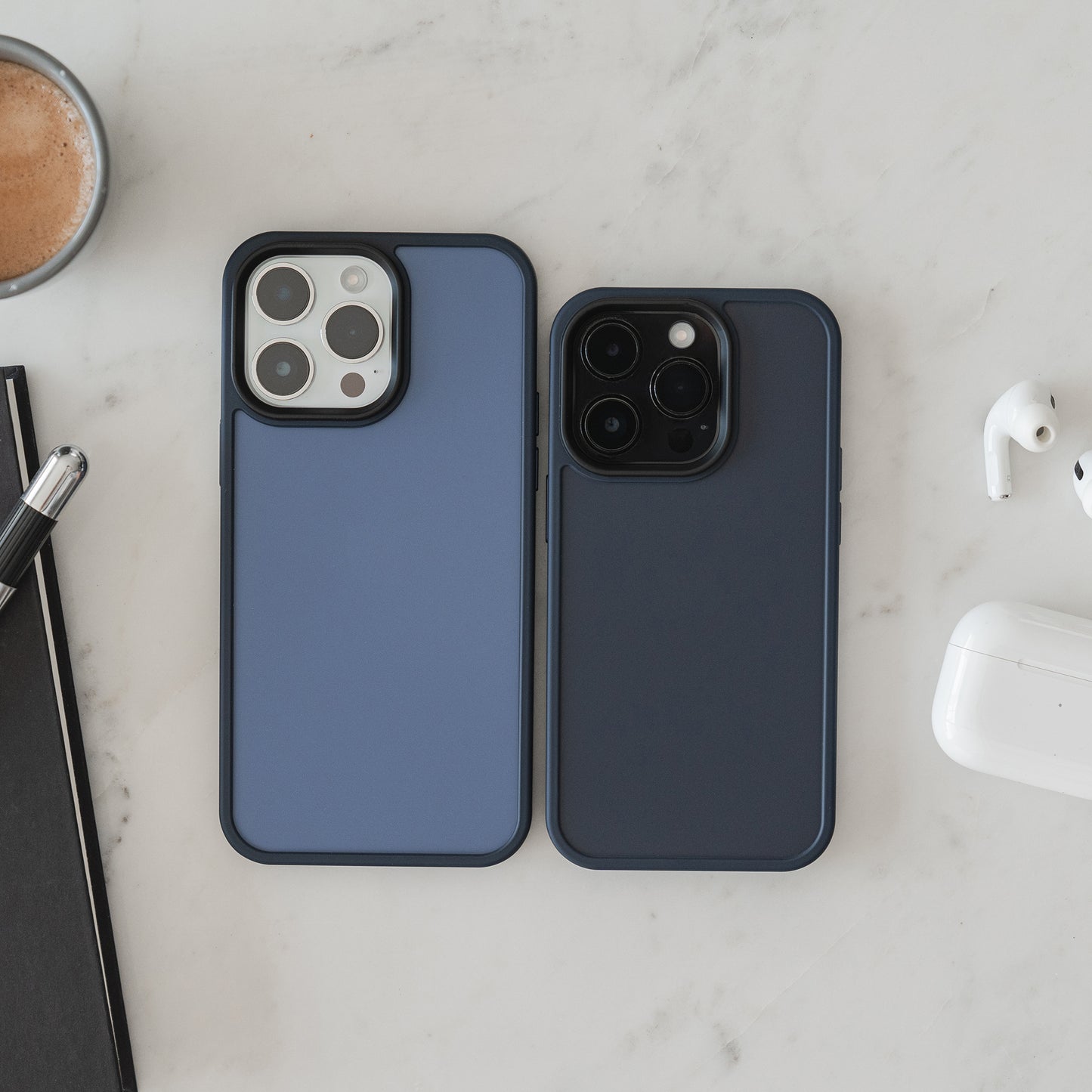 Zwei iPhones in der MR PROTECT iPhone 15 Case Matt Hülle liegen nebeneinander auf weißem Marmor, umgeben von Notizbuch, Stift, Kaffeetasse und kabellosen Kopfhörern im stoßabsorbierenden TPU-Silikon-Case von MR PROTECT.