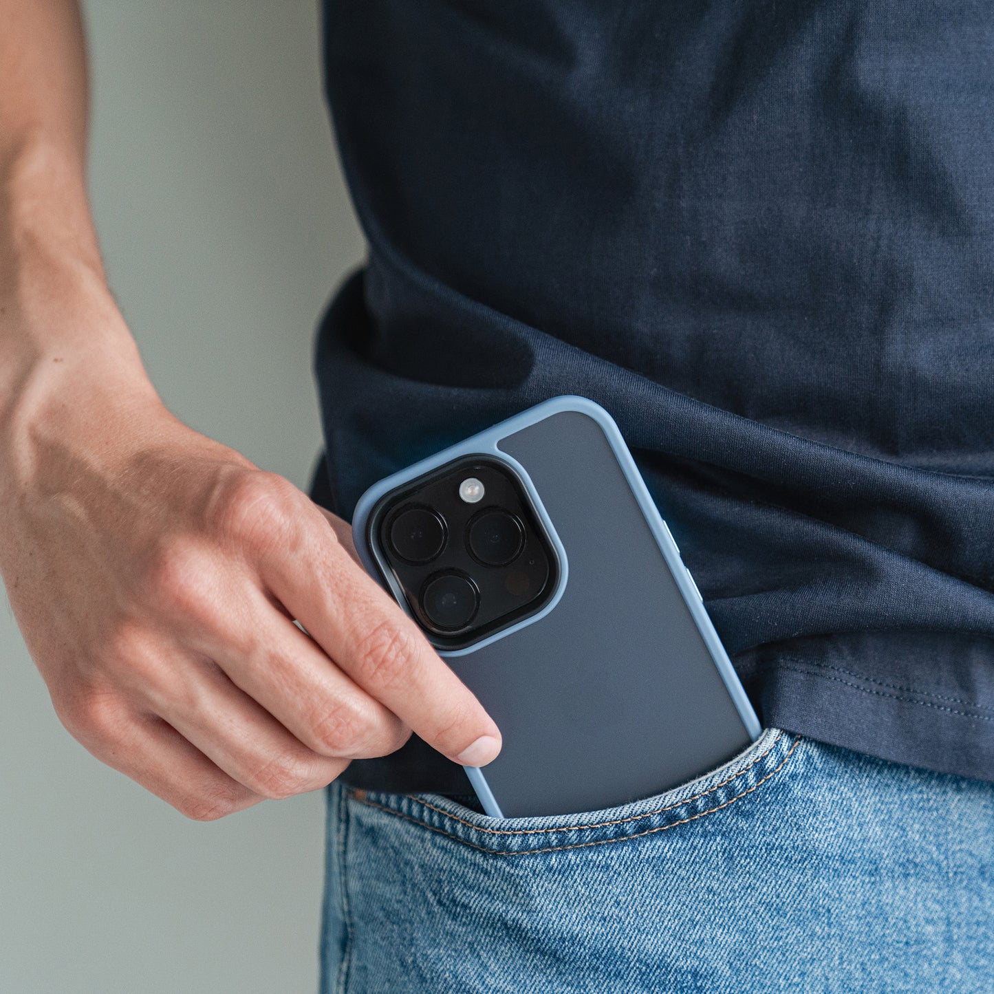 Eine Person in dunklem Hemd und Bluejeans steckt das MR PROTECT iPhone 15 Case Matt mit minimalistischem Matt-Look und sichtbarer Aussparung für die Dreifachkamera in die Vordertasche – und vereint so Stil und Stoßdämpfung.