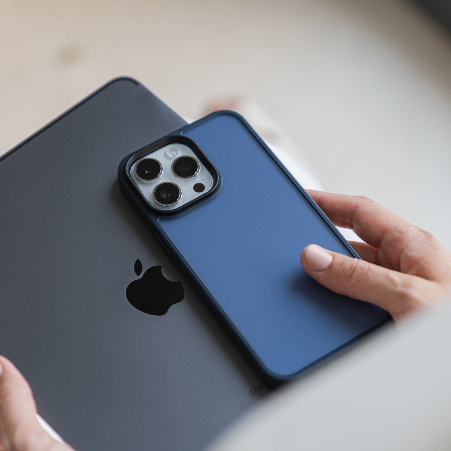 Eine Person hält ein MR PROTECT iPhone 15 Pro Case Matt in Blau und ein graues Tablet, beide zeigen auf der Rückseite das Apple-Logo. Die Hände der Person sind teilweise sichtbar.