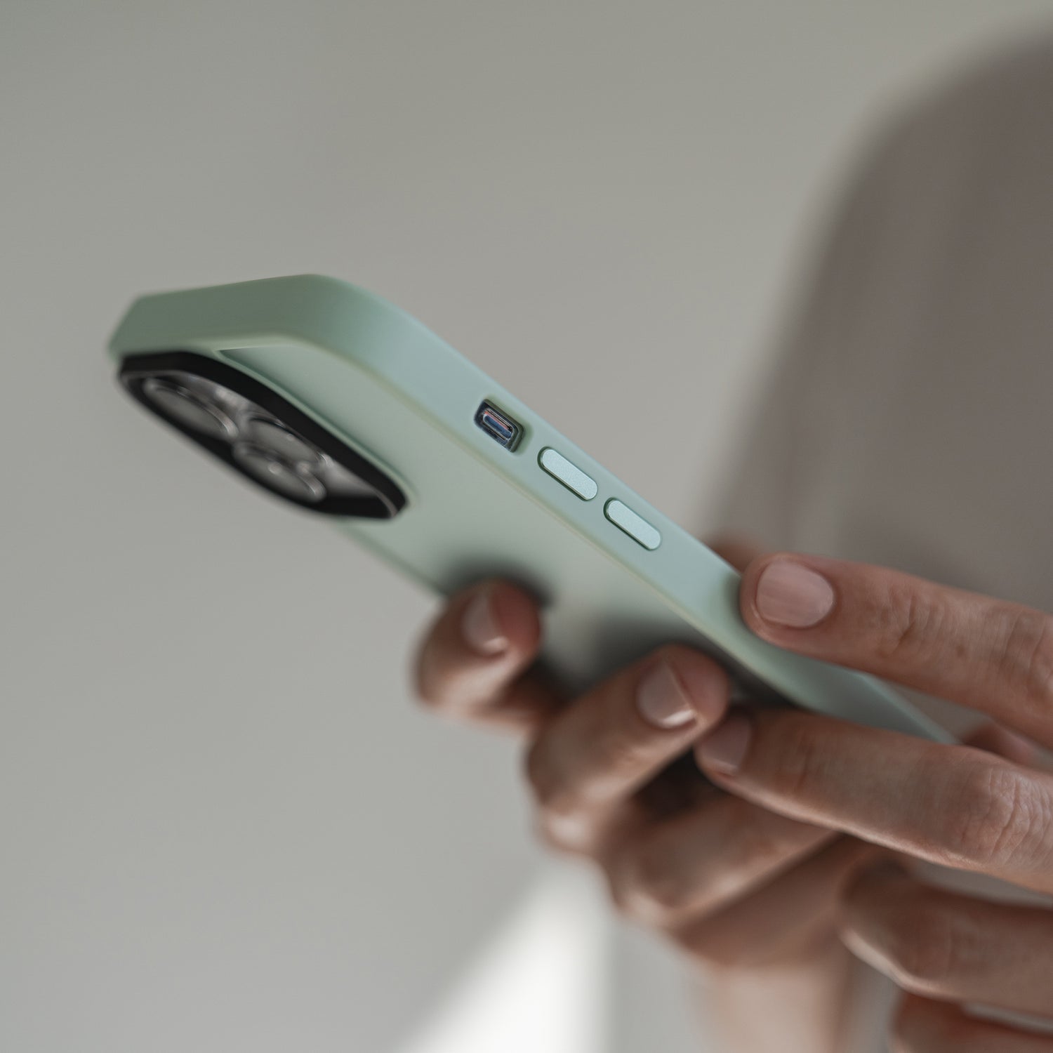 Eine Hand hält das MR PROTECT iPhone 15 Pro Case Matt in Hellgrün aus stoßdämpfendem TPU-Silikon. Seitentasten und USB-C-Anschluss sind sichtbar, mit minimalistischem Matt-Finish von MR PROTECT vor unscharfem Hintergrund.