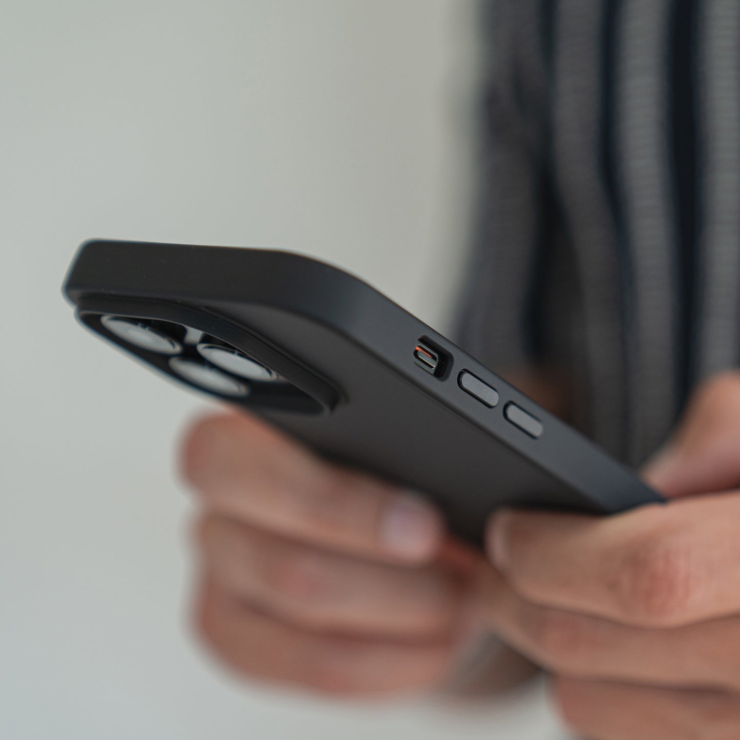 Eine Person hält das MR PROTECT iPhone 15 Pro Case Matt von MR PROTECT und hebt die seitlichen Tasten und Kameralinsen hervor. Das schwarze Case besticht durch eine stoßdämpfende TPU-Silikon-Konstruktion und einen minimalistischen, matten Look vor unscharfem Hintergrund.