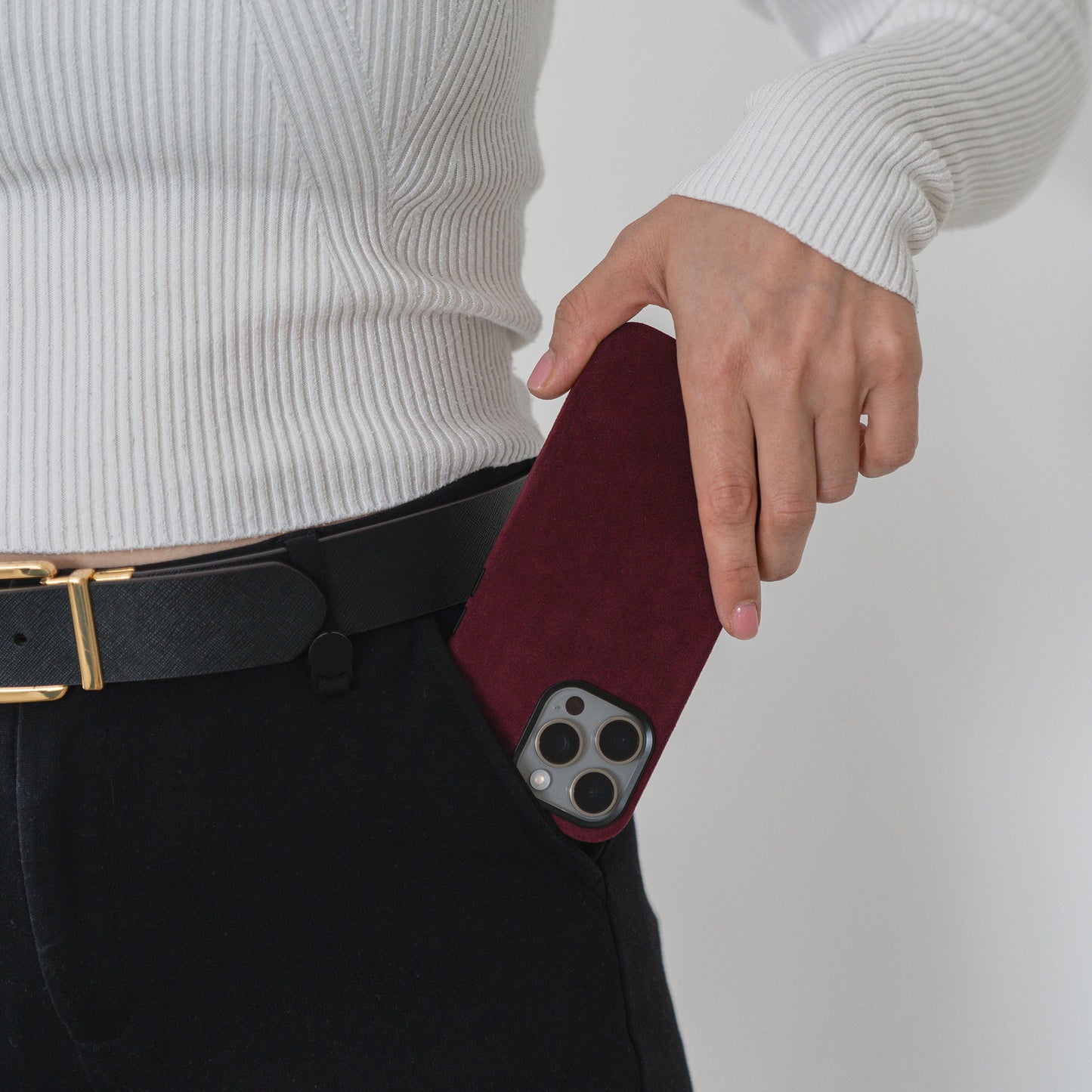 Eine Person steckt eine arktis iPhone Air Hülle aus Alcantara in Burgunderrot in die Tasche ihrer schwarzen Hose.