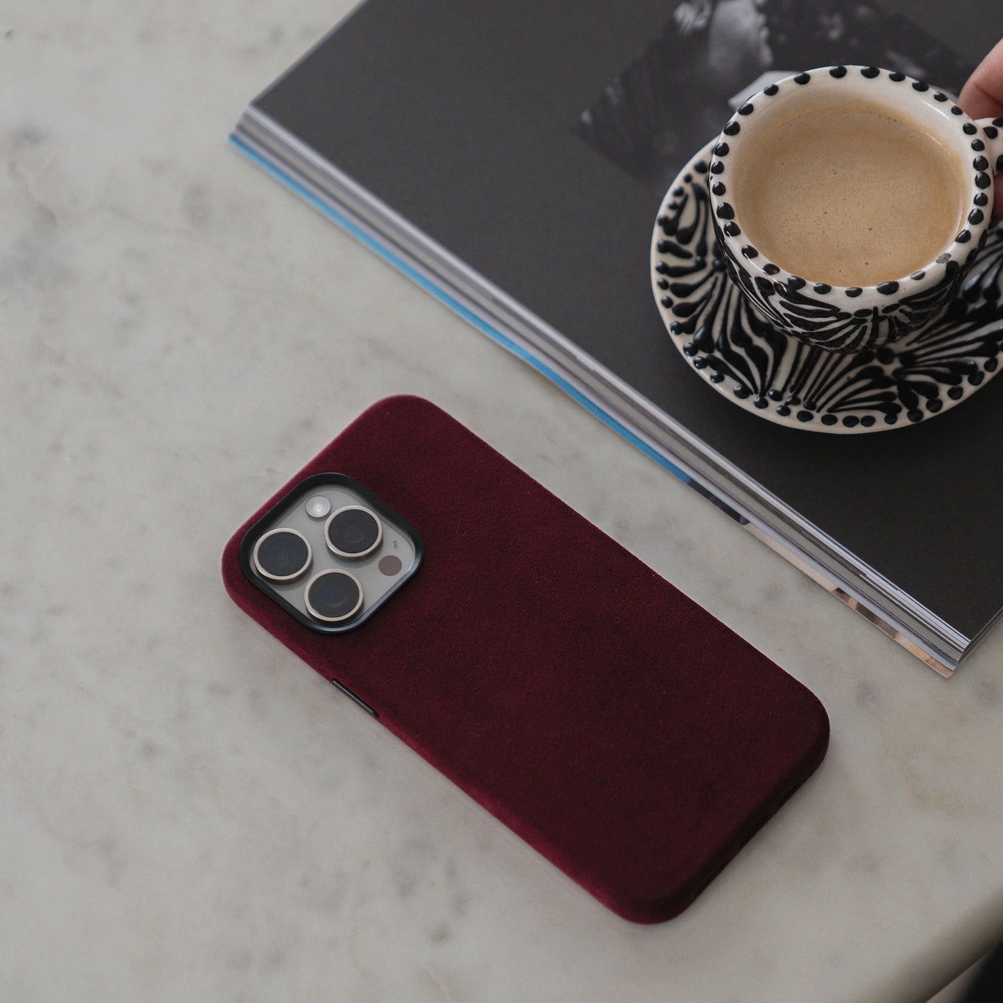 Auf einem Marmortisch liegen ein arktis iPhone Air Hülle aus Alcantara in kastanienbraun, eine Zeitschrift und eine Kaffeetasse mit Zebradruck.