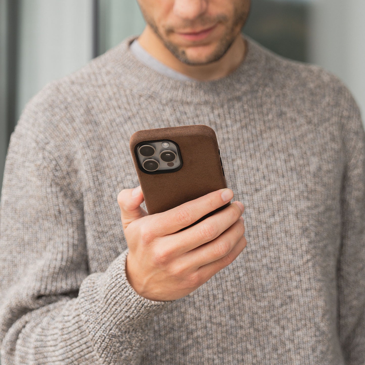 Eine Person in einem grauen Pullover hält ein arktis iPhone Air Hülle aus Alcantara in Braun und schaut konzentriert auf den Bildschirm.