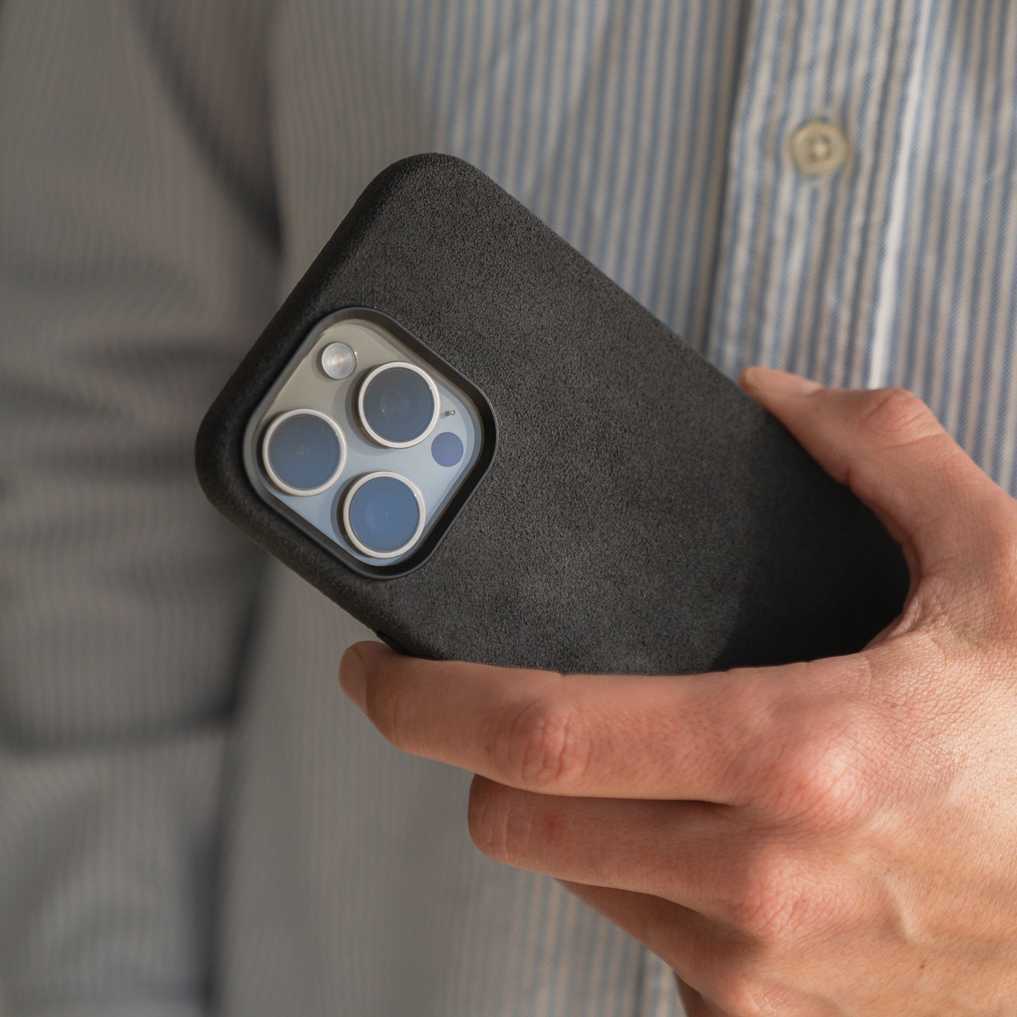 Eine Person hält ein Smartphone mit einer arktis iPhone Air Hülle aus Alcantara von arktis und trägt ein gestreiftes Hemd.