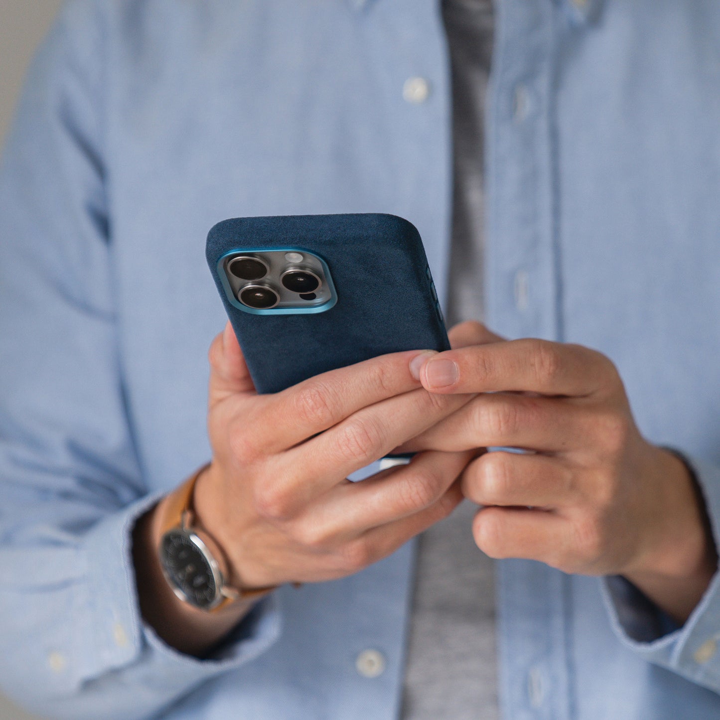 Eine Person im blauen Hemd hält ein Smartphone mit der arktis iPhone Air Hülle aus Alcantara von arktis und konzentriert sich dabei auf den Bildschirm des Telefons.