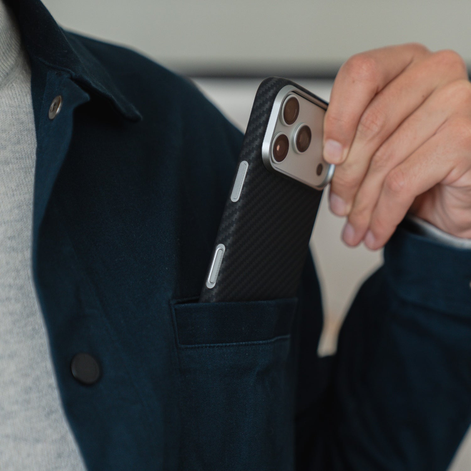 Eine Person steckt ihr iPhone 17 Pro, geschützt durch ein arktis iPhone 17 Pro Carbon Case, in ihre Jackentasche.