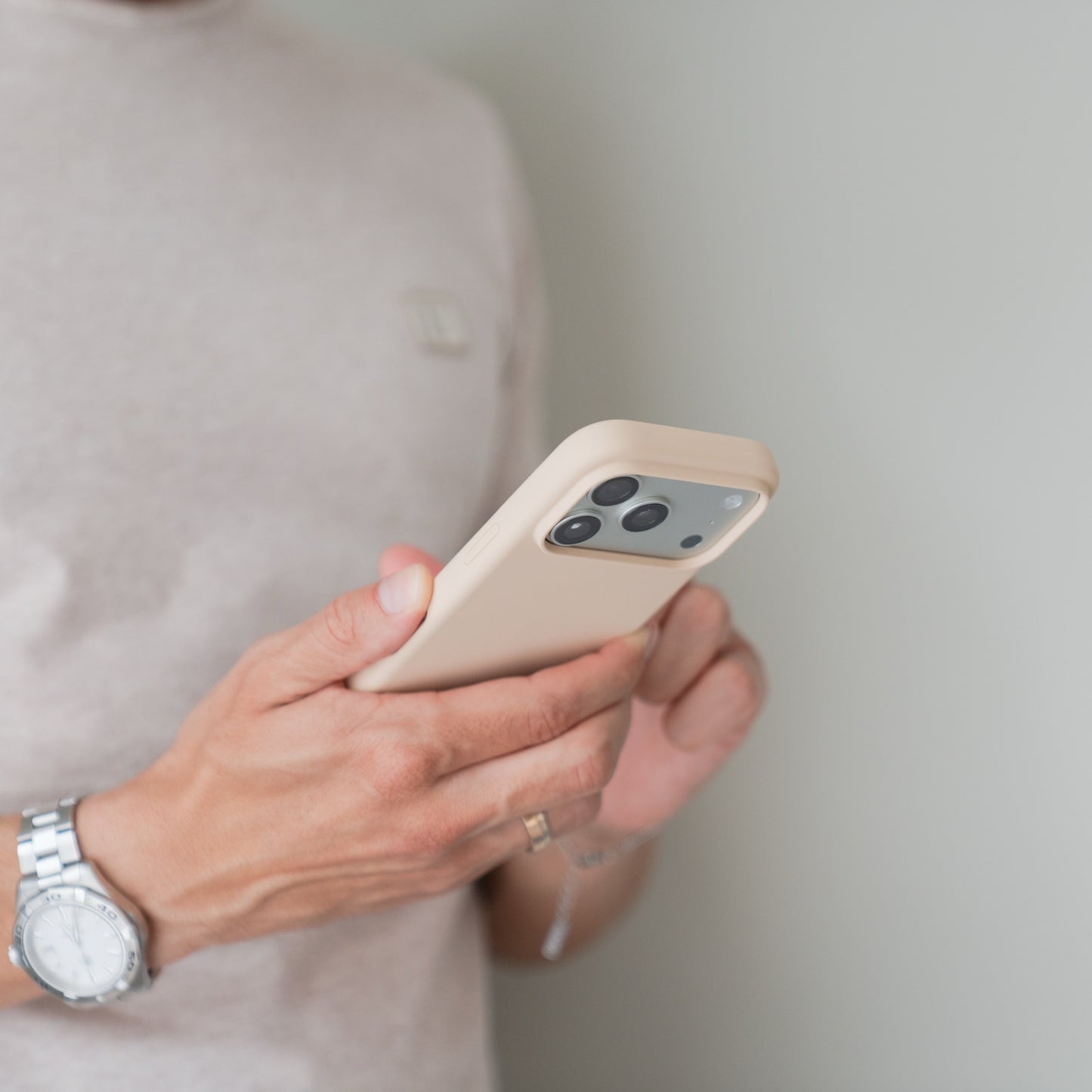 Person mit Uhr und Ring, die eine Arktis iPhone 18 Pro Max Silikonhülle mit MagSafe Polarstern in der Hand hält, vor einfarbigem Hintergrund.