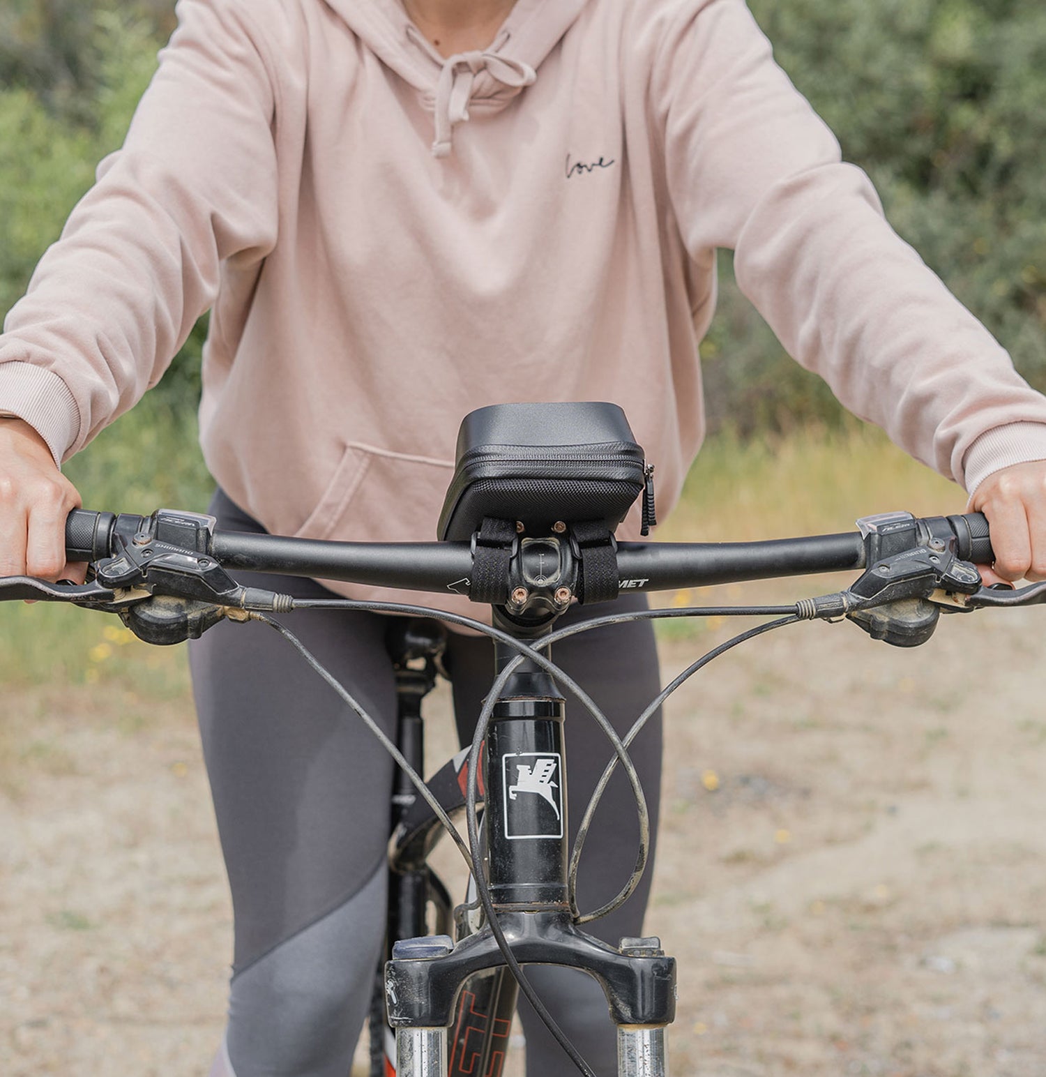 Person in einem rosa Kapuzenpullover, die im Freien Fahrrad fährt, mit einer schwarzen Tasche am Lenker.