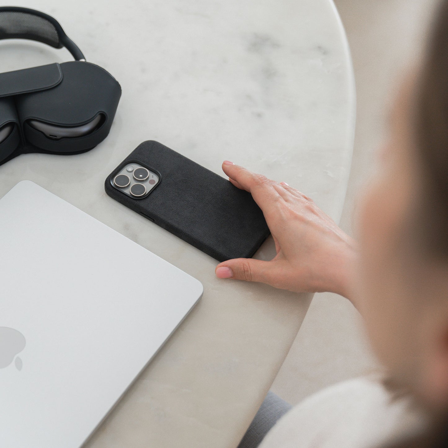 Die Hand einer Person ruht auf einem iPhone Air Hülle aus Alcantara von arktis, neben einem geschlossenen Laptop und Kopfhörern auf einem Marmortisch.
