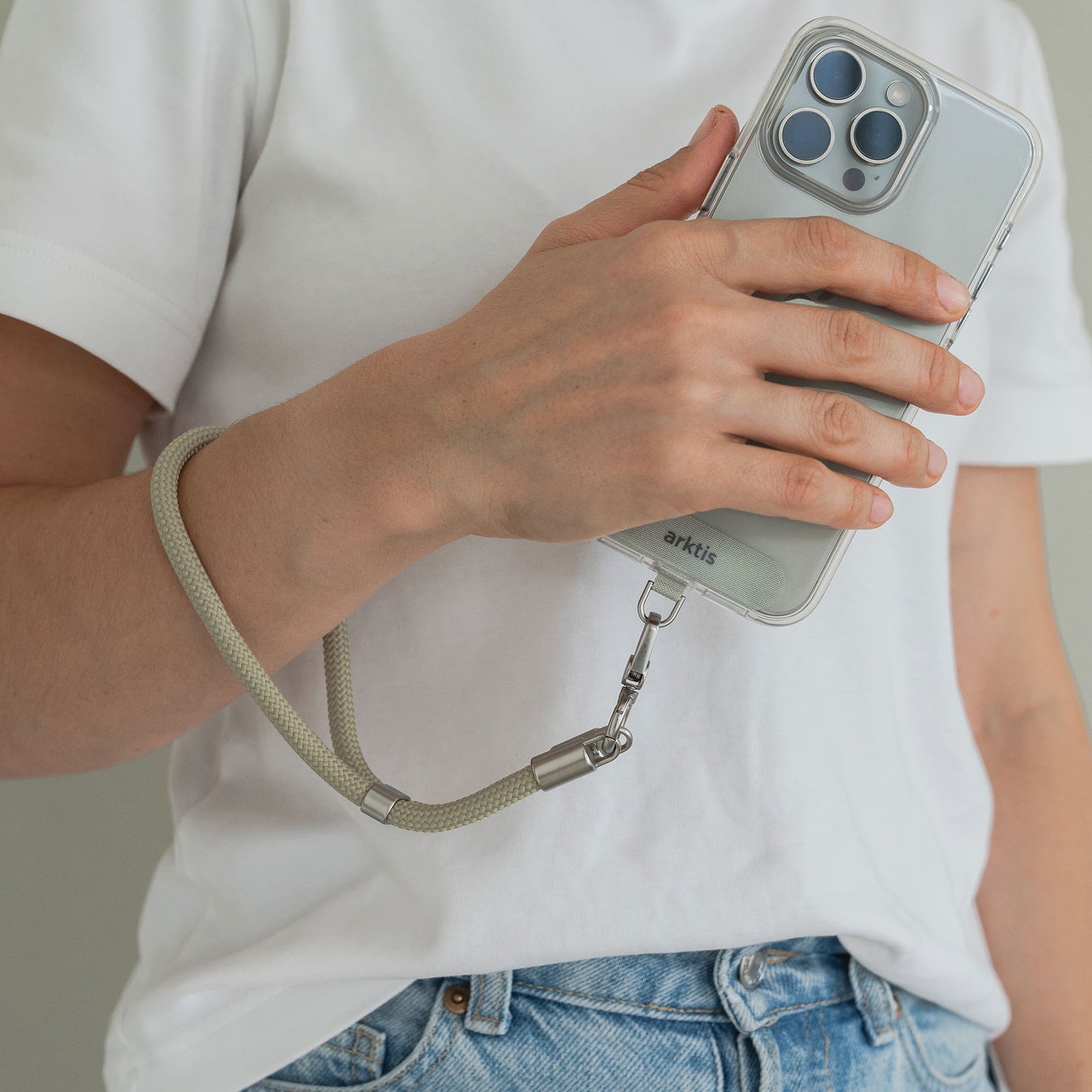 Person hält ein Smartphone mit der arktis Lanyard Handykette fürs Handgelenk von Arktis, mit verstellbarer Länge, kombiniert mit einem weißen T-Shirt und blauen Jeans – ein stylisches Smartphone-Accessoire für den täglichen Gebrauch.