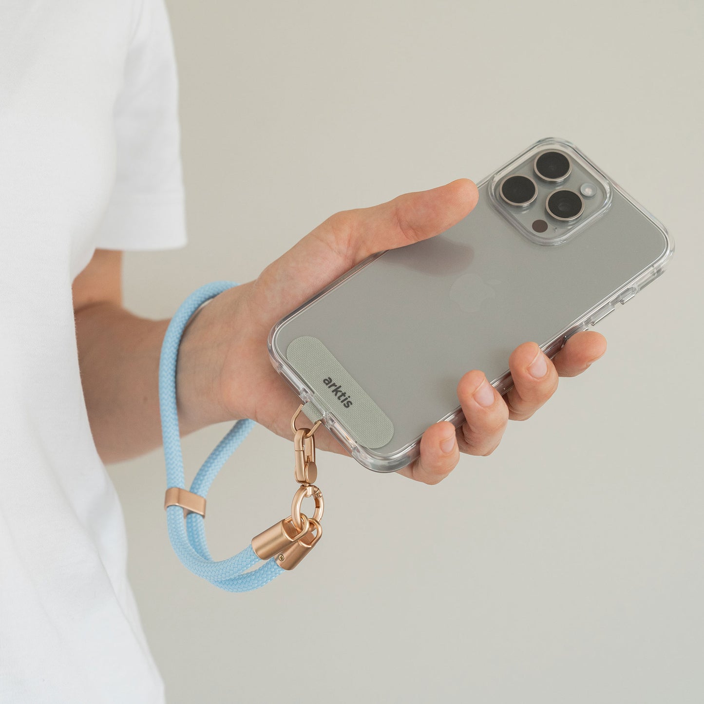 Person, die ein Smartphone mit einem Arktis-Lanyard hält. Handykette fürs Handgelenk von Arktis – diese stilvolle Handgelenkschlaufe ist das ideale Mode-Accessoire für Ihre Smartphone-Zubehör-Sammlung.