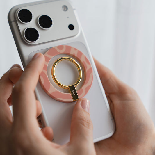 Eine Hand hält ein weißes Telefon mit dem arktis Magnetischer Ringhalter für MagSafe - Sweet Leopard in Pink und Gold, der stylisches iPhone Zubehör und starke N52 Magnete für einen sicheren Halt kombiniert.