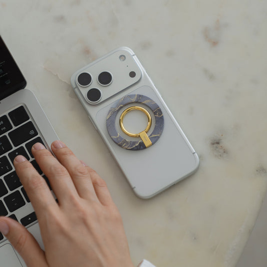 Eine Hand tippt auf einem Laptop neben einem Smartphone mit dem arktis Magnetischer Ringhalter für MagSafe - Sweet Leopard, einem eleganten und funktionalen iPhone Zubehör mit N52 Magnete auf einer weißen Oberfläche.