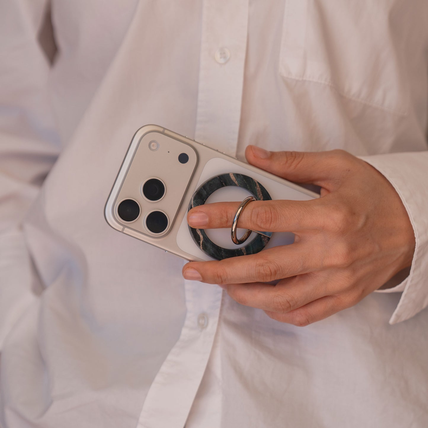 Eine Person in einem weißen Hemd hält ein iPhone, an dem der arktis Magnetischer Ringhalter für MagSafe - Sweet Leopard befestigt ist, und hebt damit dieses stilvolle Zubehör hervor.