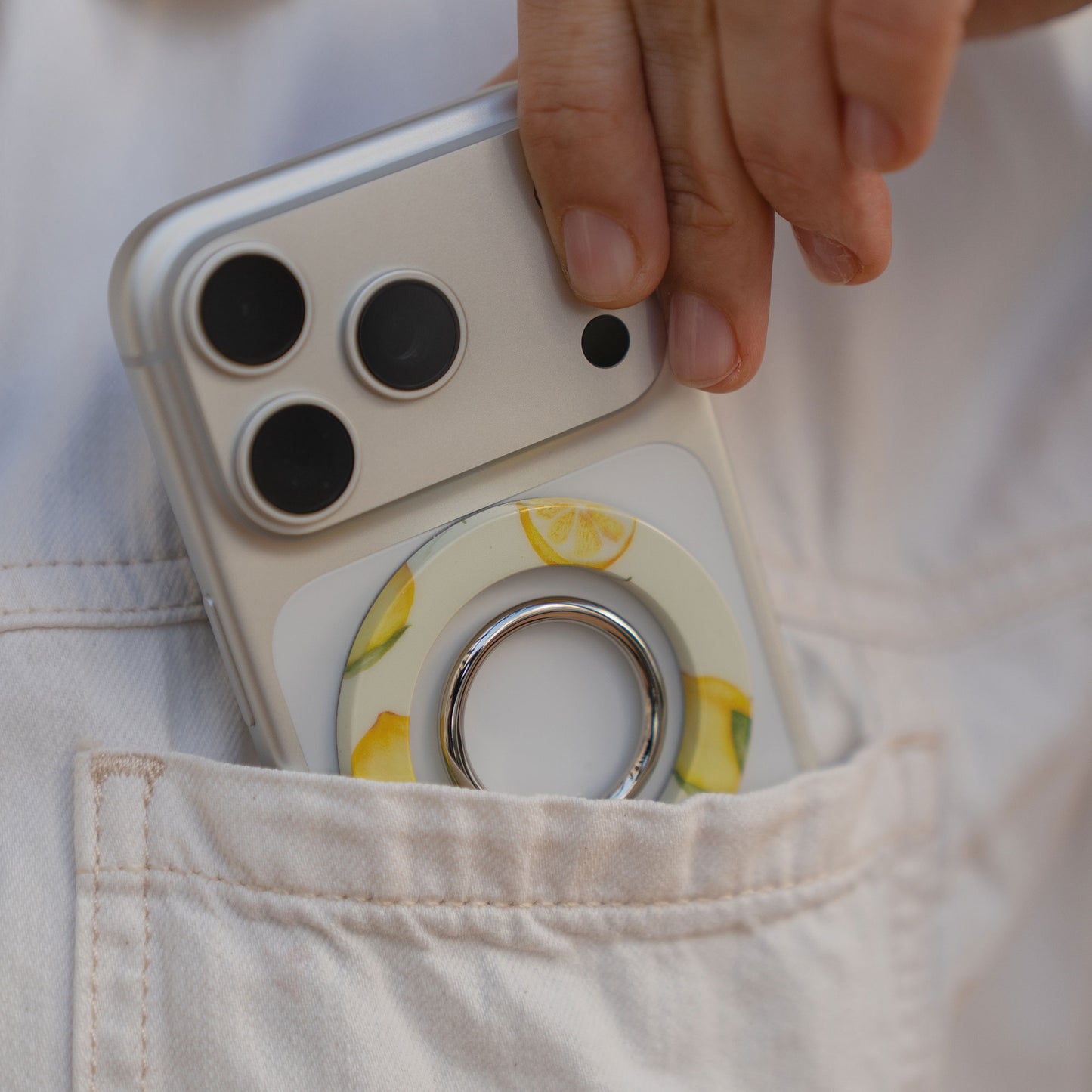 Eine Hand legt ein silbernes Telefon mit dem arktis Magnetischer Ringhalter für MagSafe - Sweet Leopard in ein leichtes, taschenähnliches iPhone Zubehör mit starken N52 Magneten zur sicheren Befestigung.