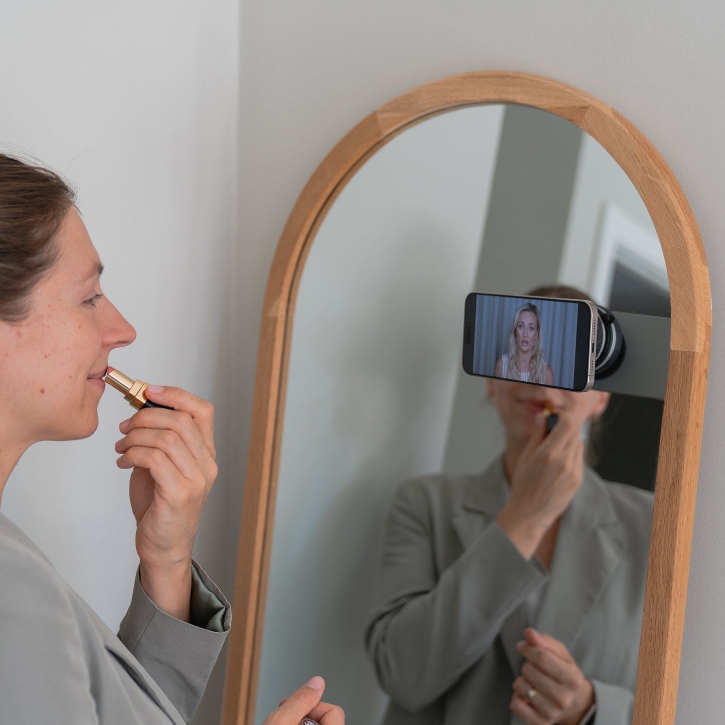 Eine Frau trägt vor einem Spiegel Lippenstift auf, während ihr iPhone, gehalten von der arktis MagicDock iPhone MagSafe Halterung von arktis, ihr Spiegelbild aufnimmt.