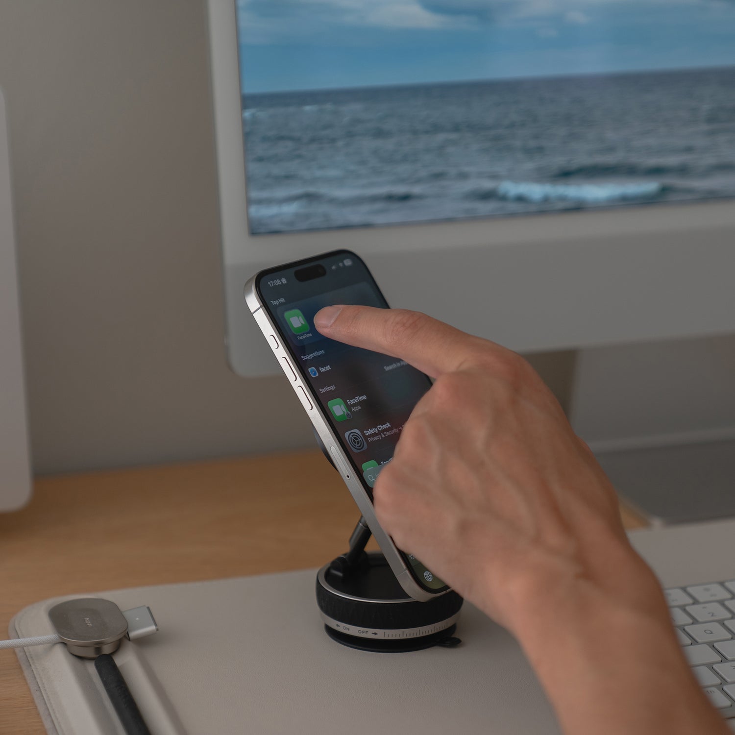 Eine Hand berührt ein iPhone auf der arktis MagicDock iPhone MagSafe Halterung, die vor einem Computermonitor steht, der das Meer zeigt.