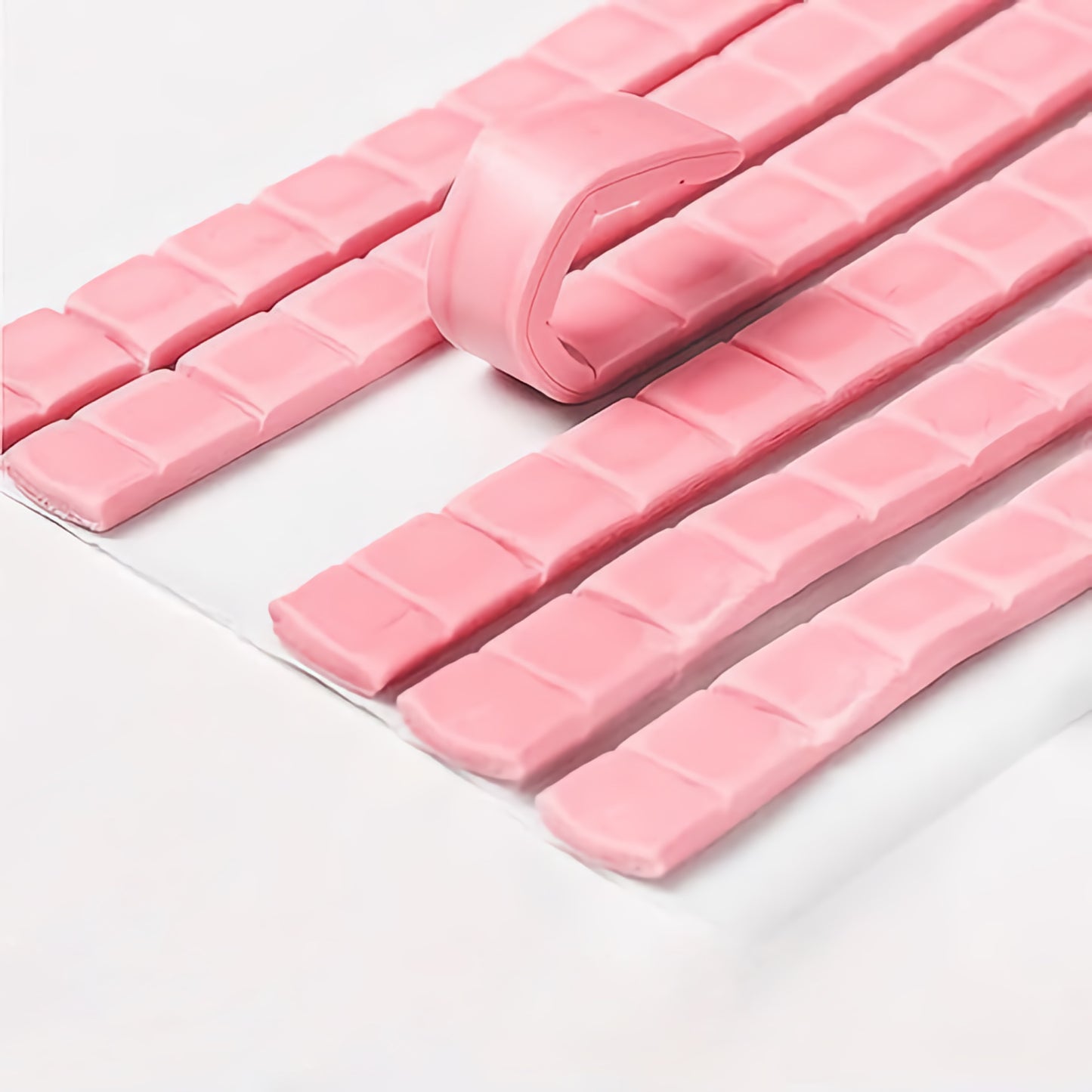 Vier Reihen von arktis Reinigungskneten für iPhone, iPad und Apple Watch von arktis, jeweils aus verbundenen rosa rechteckigen Teilen, sind auf einer weißen Oberfläche angeordnet, wobei eine Reihe zur besseren Darstellung oben teilweise eingerollt ist.