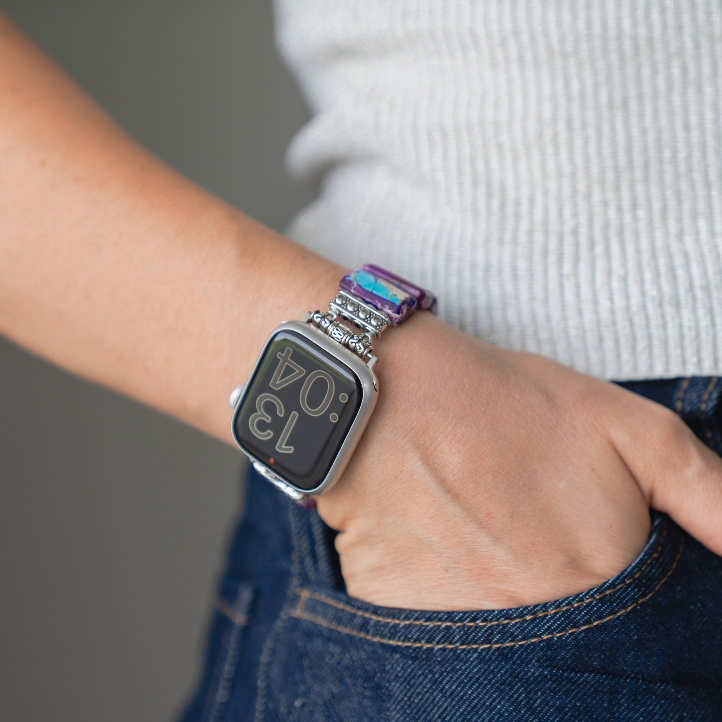 Eine Person trägt die Apple Watch "Stone Loop" von arktisband mit einem bunten Band und der Anzeige 13:04 mit der Hand in der Tasche.