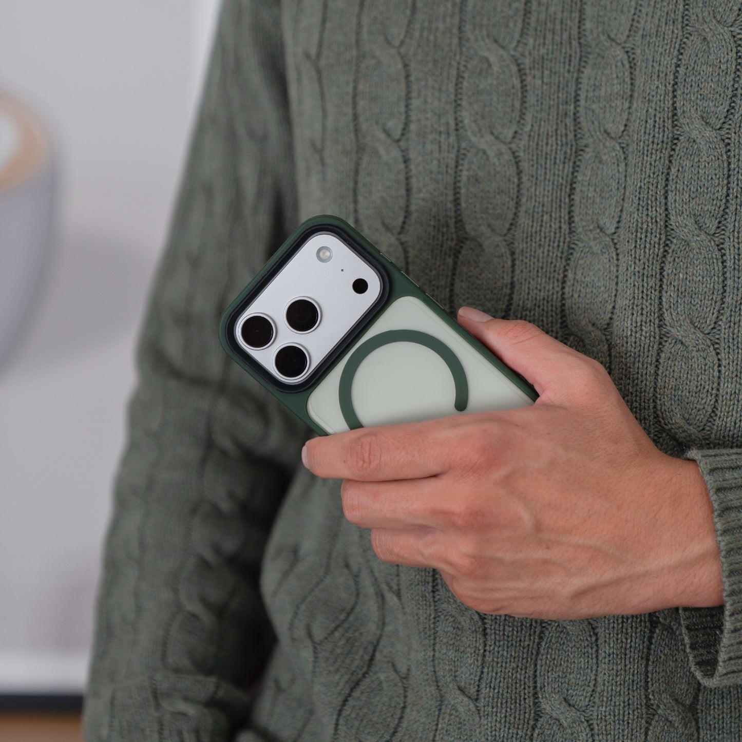 Eine Person in einem grünen Pullover hält ein Smartphone mit einem Arktis iPhone 17 Pro Solid Case mit MagSafe.