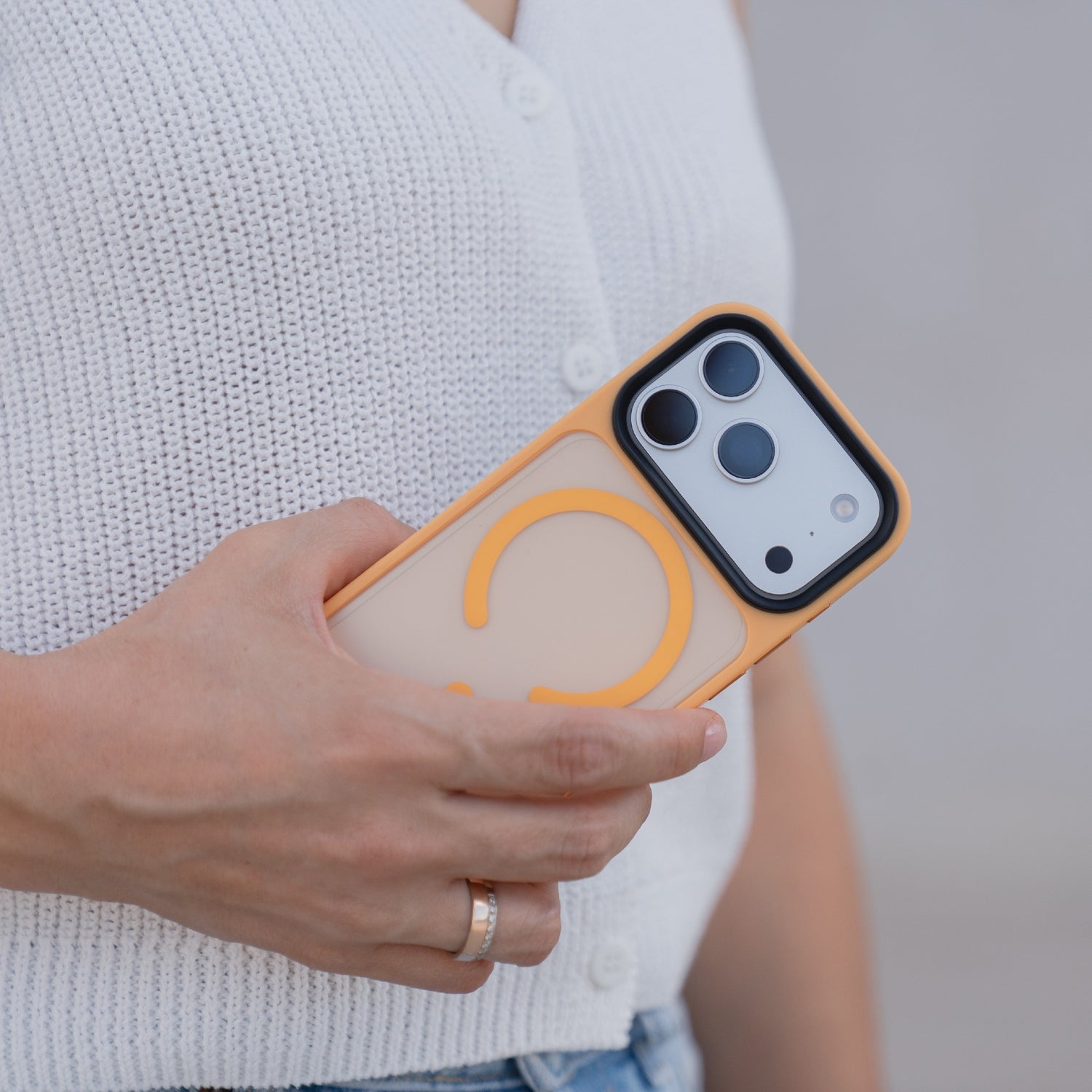 Eine Person in einem weißen Strickoberteil hält ein iPhone 17 Pro mit dem Arktis iPhone 17 Pro Solid Case mit MagSafe in Pfirsich und Gelb, einer matten, MagSafe-kompatiblen Hülle von Arktis.