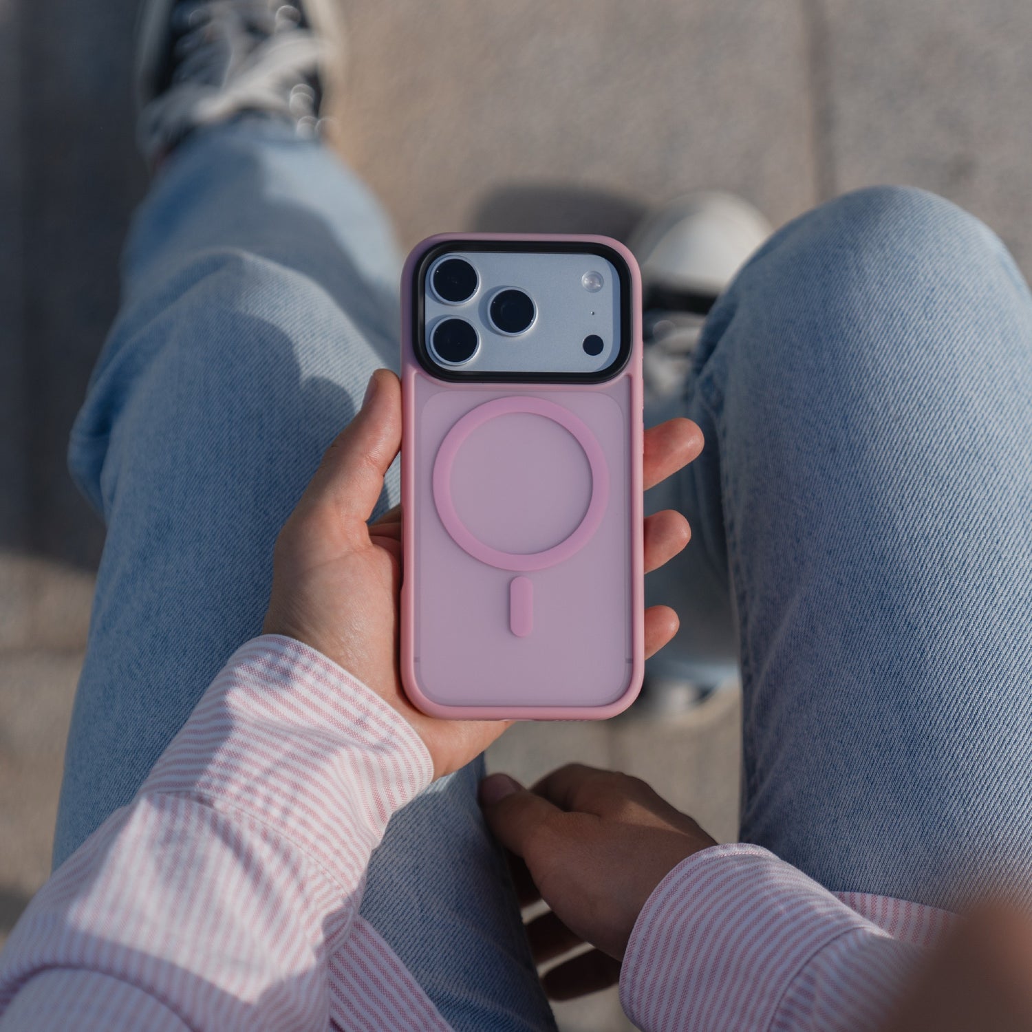 Eine Person in Jeans hält ein Arktis arktis iPhone 17 Pro Solid Case mit MagSafe in rosa, im Freien sitzend.
