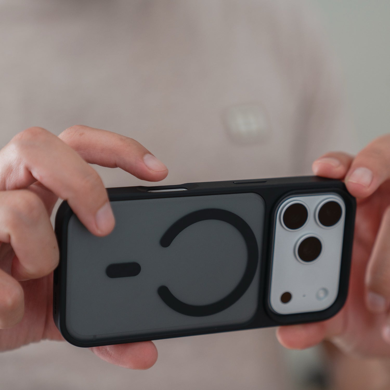 Eine Person hält das Arktis iPhone 17 Pro Solid Case mit MagSafe, eine schwarz-graue, matte Schutzhülle von Arktis mit einem runden, MagSafe-kompatiblen Design auf der Rückseite.
