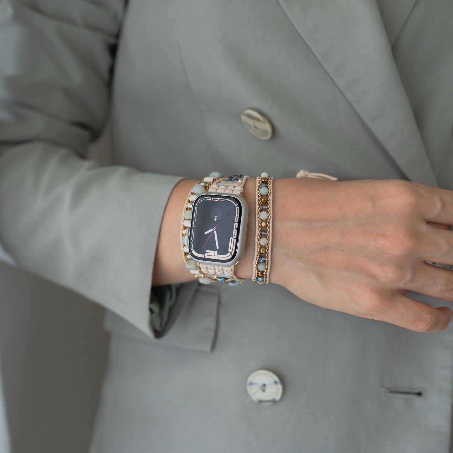 Eine Person in einem grauen Blazer trägt das arktisband Apple Watch Armband "Dream Catcher" von arktisband und ein Perlenarmband an ihrem Handgelenk.