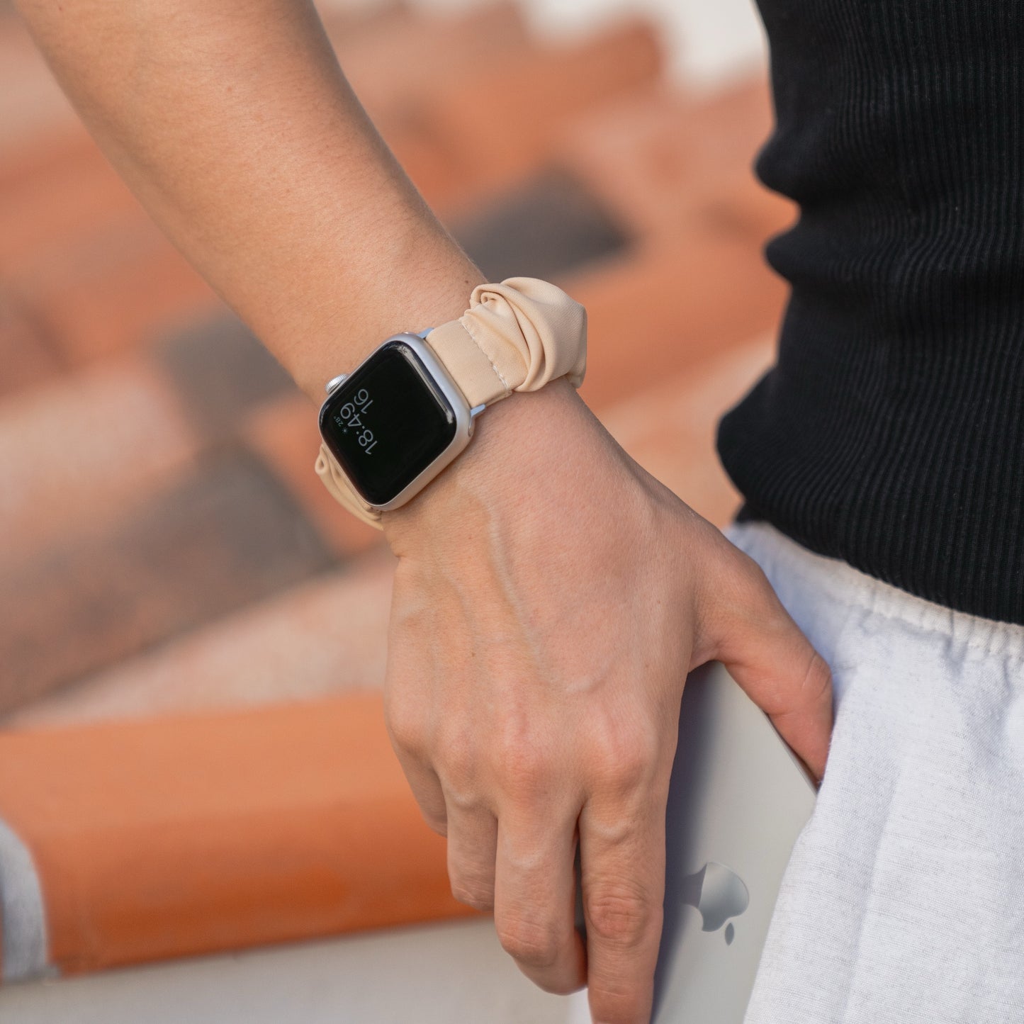 Nahaufnahme des Handgelenks einer Person, die das Arktisband Apple Watch Scrunchie Armband "Elanora" mit beigem Band trägt, in der Nähe von Terrakotta-Stufen.