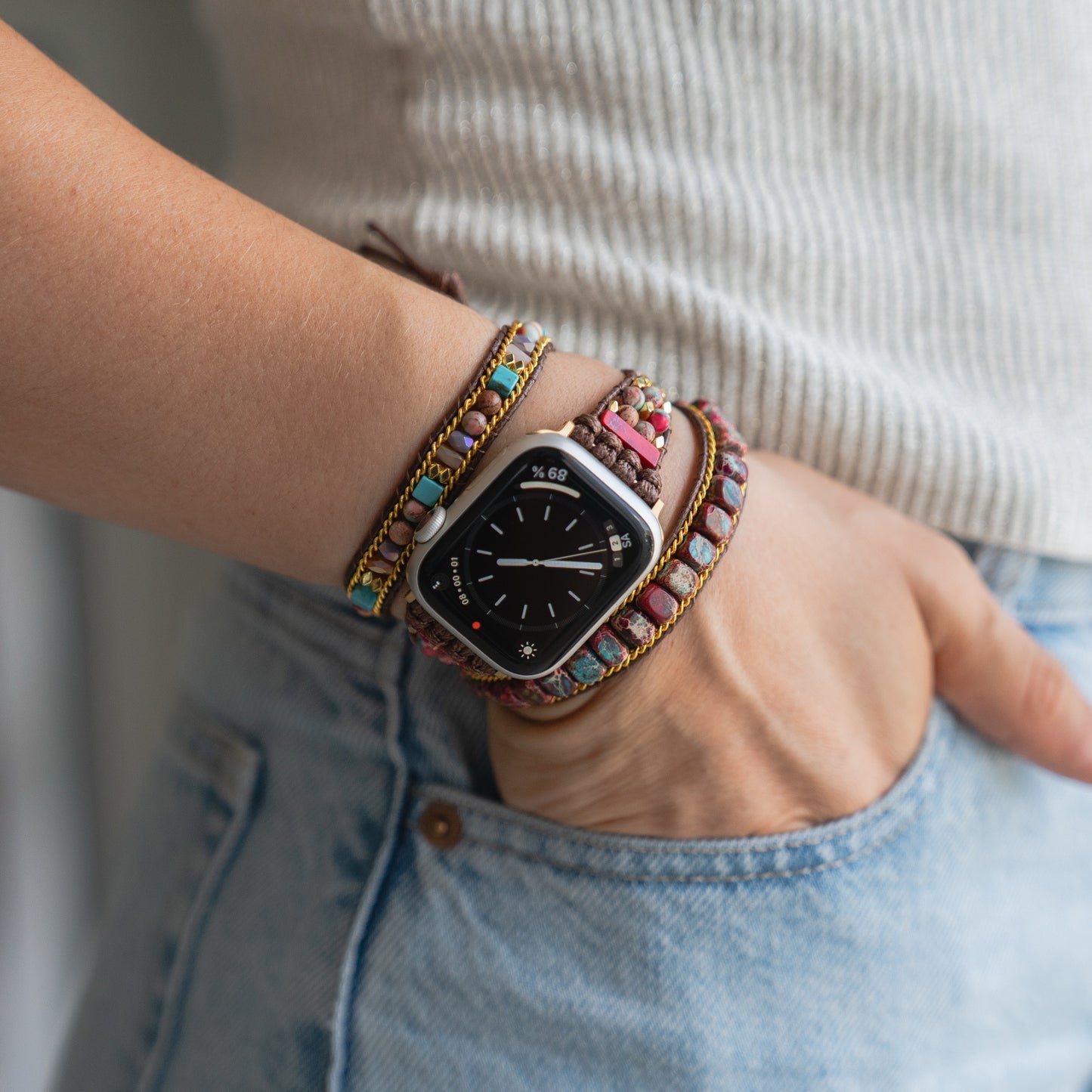 Eine Person trägt bunte Perlenarmbänder und das arktisband Apple Watch Armband "Dream Catcher" von arktisband, ihre Hand steckt in einer blauen Jeanstasche.