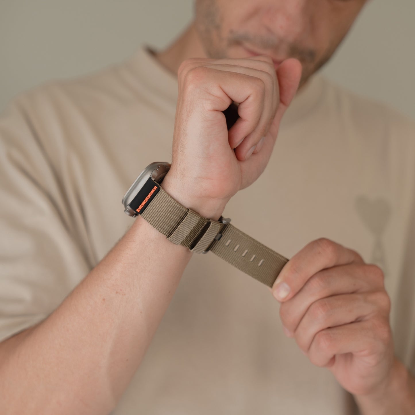 Eine Person befestigt ein olivgrünes Arktisband Apple Watch Armband "Terra" an ihrem Handgelenk, während sie ein beiges Hemd trägt.