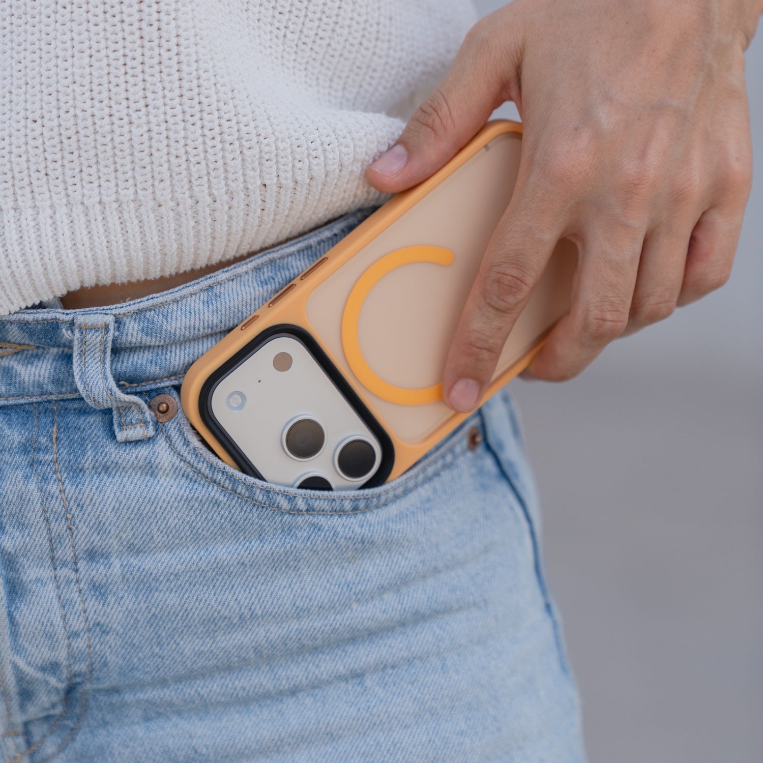 Eine Person steckt ein Arktis iPhone 17 Pro Solid Case mit MagSafe in orange matt in die Vordertasche einer hellblauen Jeans.