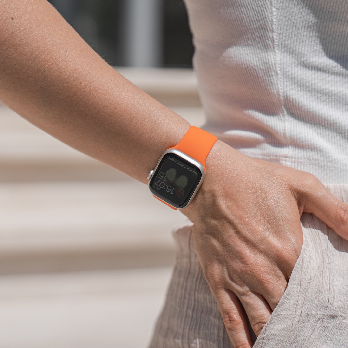 Eine Person im Freien trägt ein weißes ärmelloses Oberteil und einen leichten Rock, während das Sonnenlicht ihren Arm hervorhebt, der mit dem arktisband Apple Watch Silikonarmband „Aqua“ von arktisband geschmückt ist.