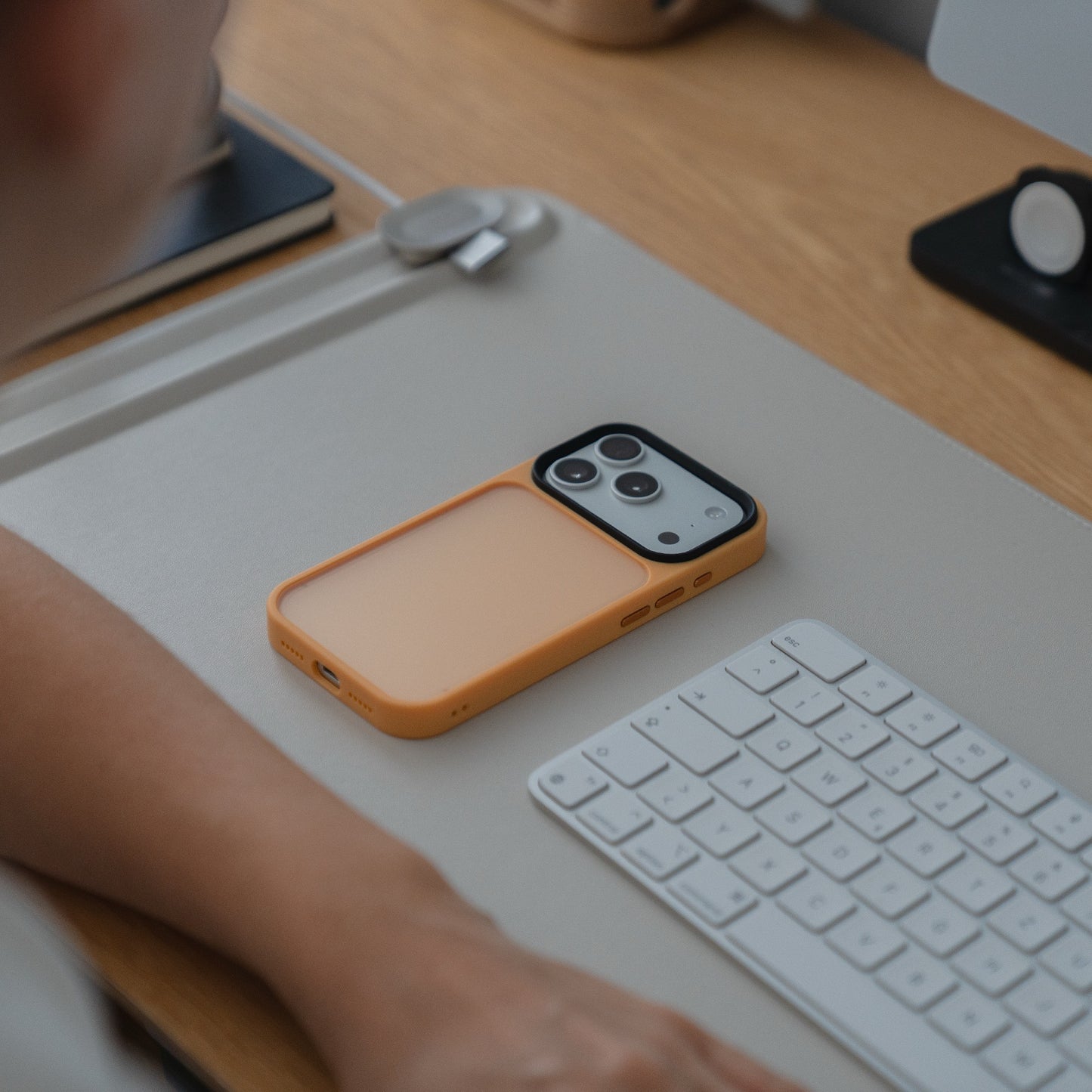 Das Arktis iPhone 17 Pro Solid Case aus stoßabsorbierendem TPU-Silikon liegt matt auf einem Schreibtisch neben einer Tastatur und dem Arm einer Person.