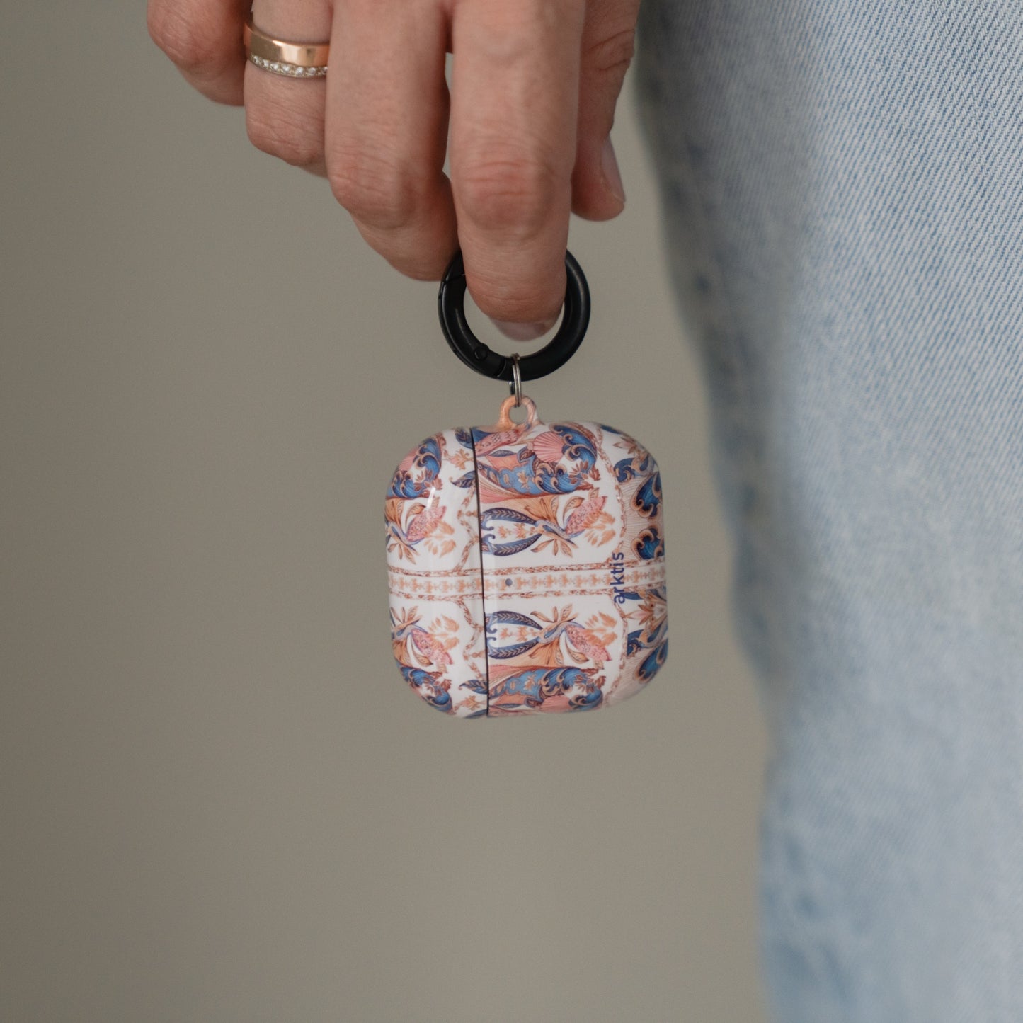 Eine Hand, die eine Arktis AirPods 5-Hülle – Peacock Palace – mit einem kunstvollen Blumenmuster in Blau, Orange und Weiß hält.