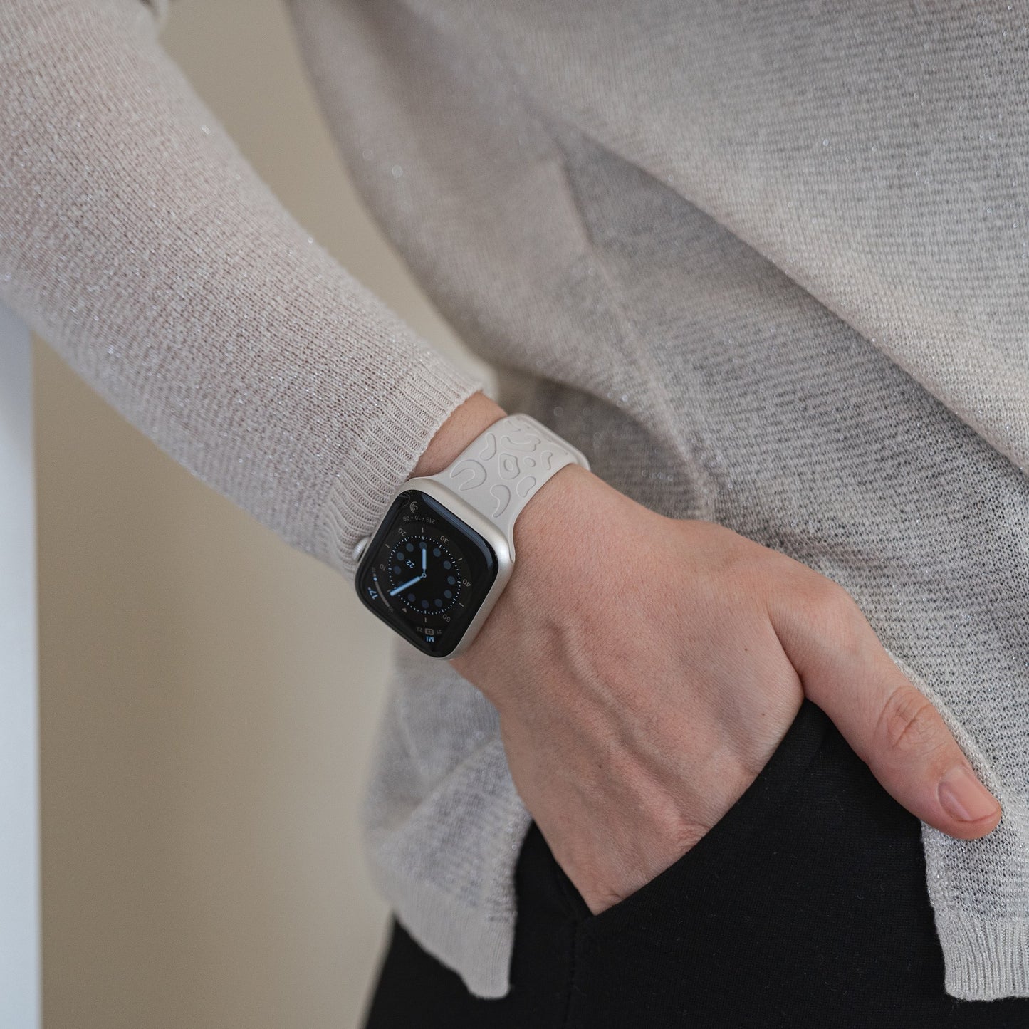 Eine Person trägt das arktisband Apple Watch Armband „Leopard“ am linken Handgelenk, die Hand in der Tasche einer schwarzen Hose und kombiniert es mit einem hellbeigen, langärmeligen Strickoberteil.