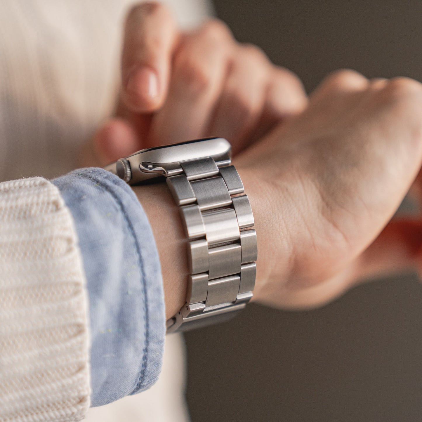 Nahaufnahme eines linken Handgelenks mit dem arktisband Apple Watch Gliederarmband „Prime“ von arktisband mit Gliederarmband; die rechte Hand stellt die Uhr ein. Die Person trägt einen weißen Pullover und ein blaues Hemd.