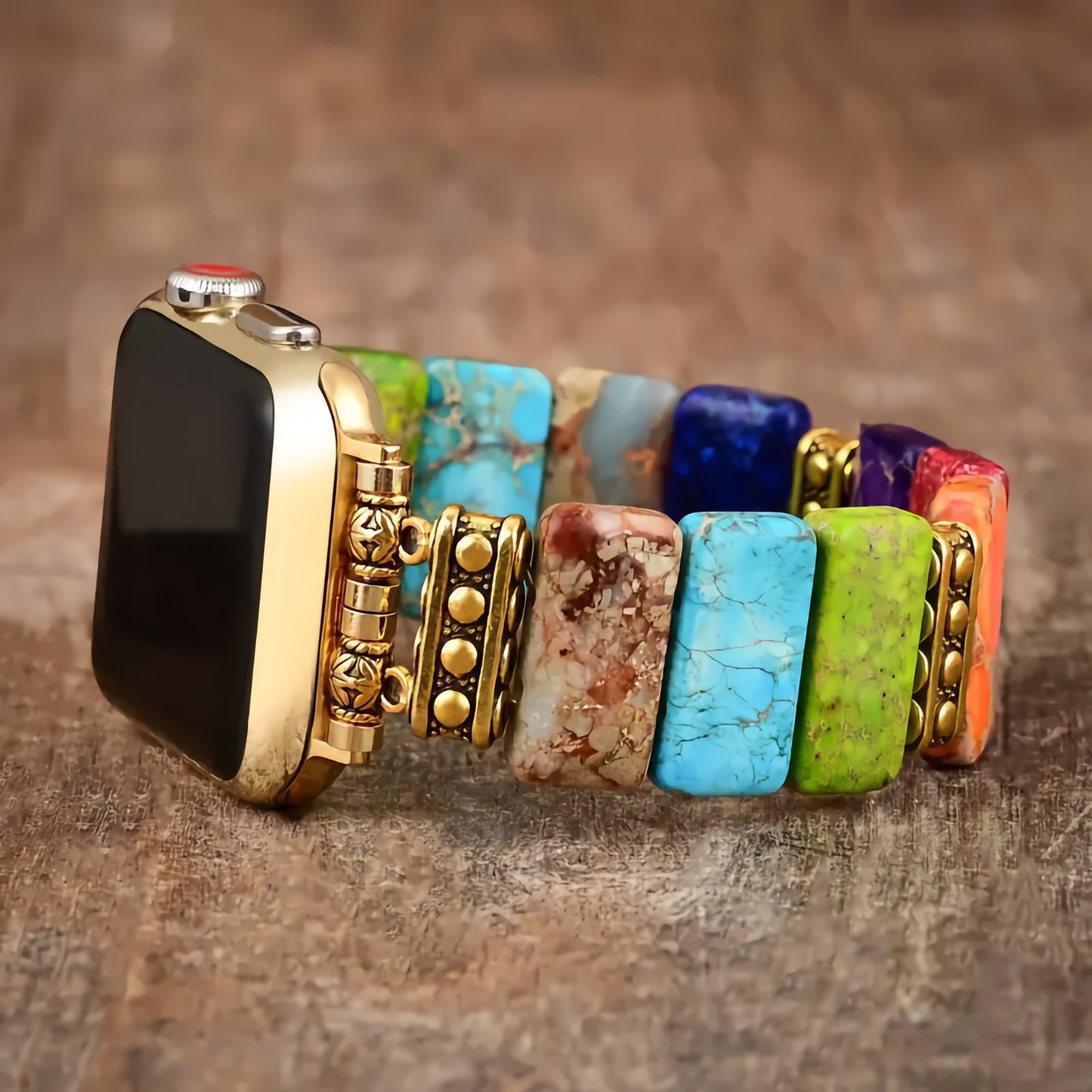 Die arktisband Apple Watch „Stone Loop“ von arktisband verfügt über ein farbenfrohes Armband aus Naturstein und Goldperlen, Apple Watch-kompatibel, das auf einer Holzoberfläche präsentiert wird.