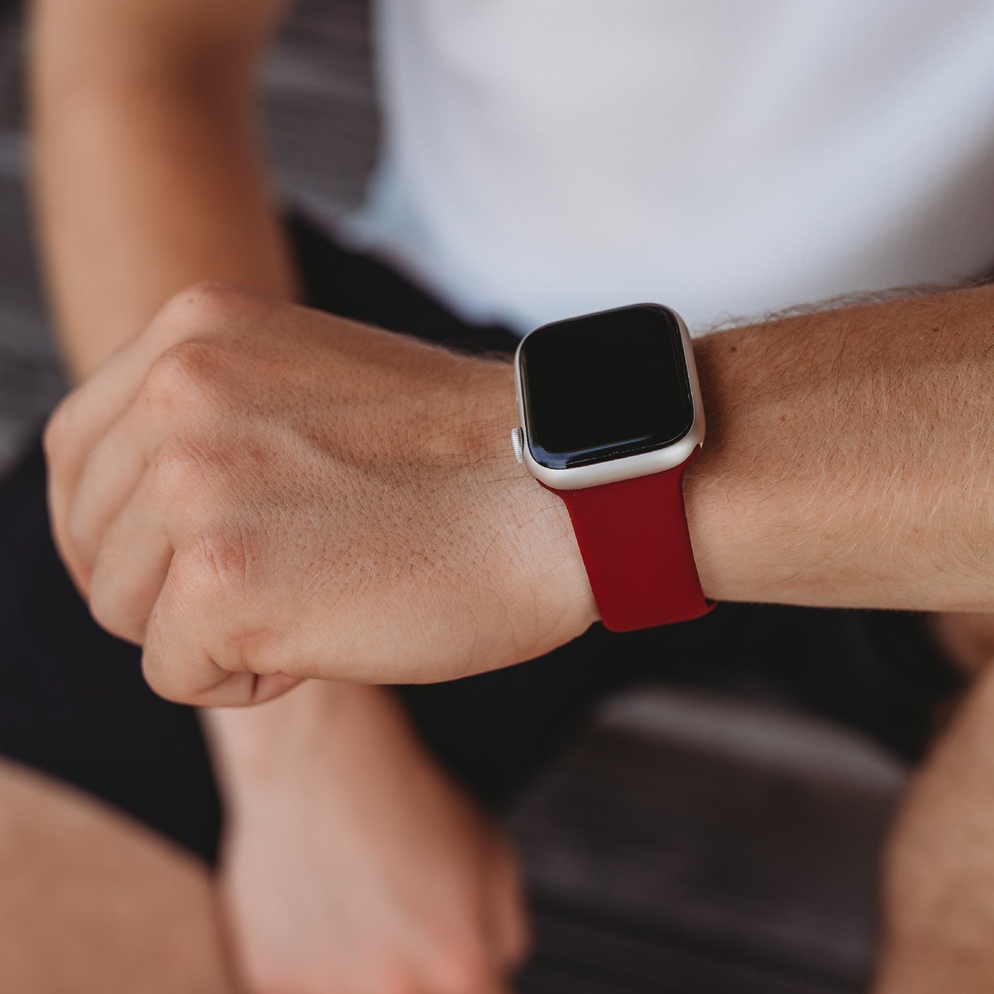 Eine Person trägt ein Arktisband Apple Watch Silikonarmband „Aqua“ am linken Handgelenk, wobei der Bildschirm der Smartwatch leer ist, und ist mit einem weißen Hemd und schwarzen Shorts bekleidet.