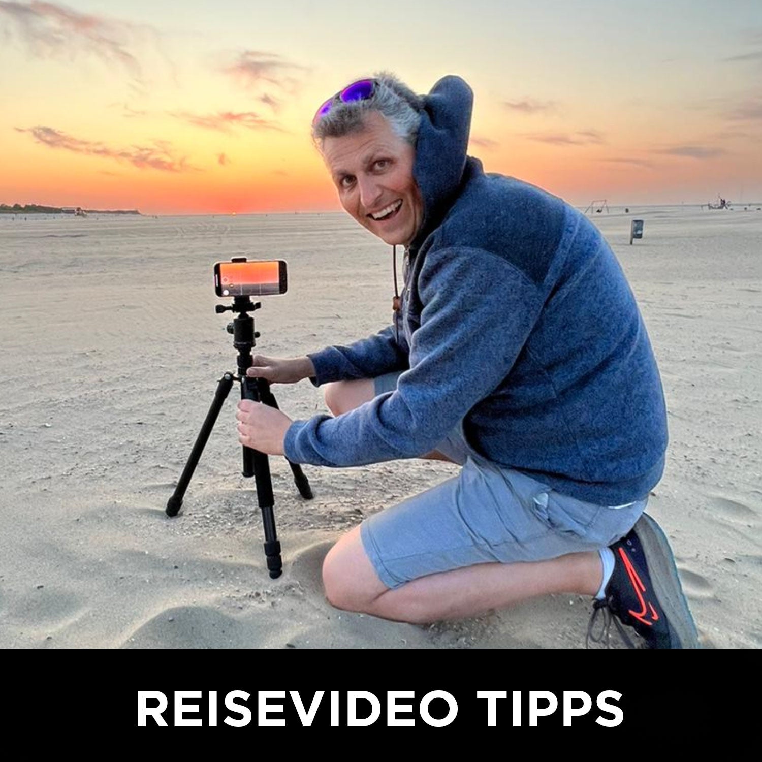 Ein Mann stellt bei Sonnenuntergang sein iPhone auf einem Stativ am Strand auf und lächelt. Text lautet: REISEVIDEO TIPPS – perfekt für alle, die ihre Videos mit dem Online Kurs „Filmen mit dem iPhone“ von Rainer Wolf verbessern wollen.