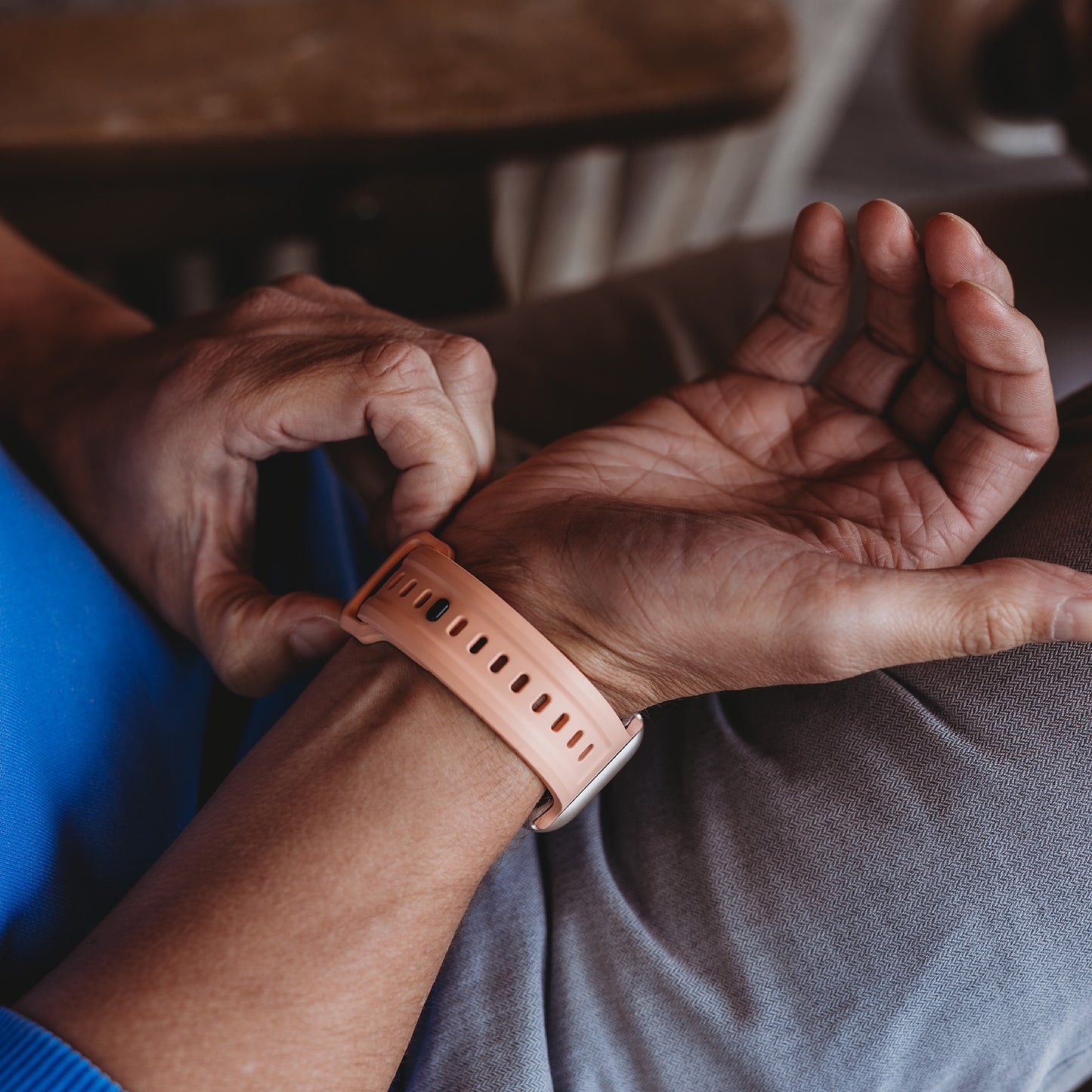 Eine Person trägt das arktisband Apple Watch FKM Sportarmband „Sweat“ in Peach am Handgelenk. Das flexible, strapazierfähige Band von artisband ist kompatibel mit der Apple Watch. Sie trägt graue Hosen und ein blaues Hemd.